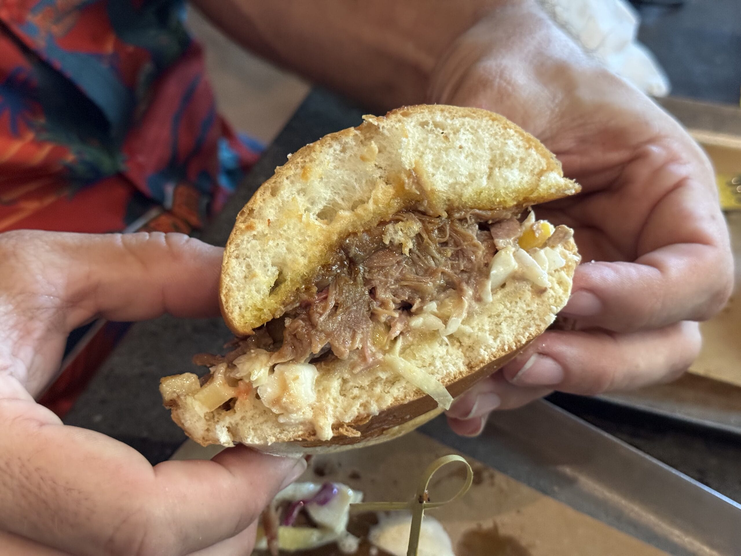 A person holds a pulled pork sandwich with coleslaw on a toasted bun at The Oak & Star Tavern, ready to eat.