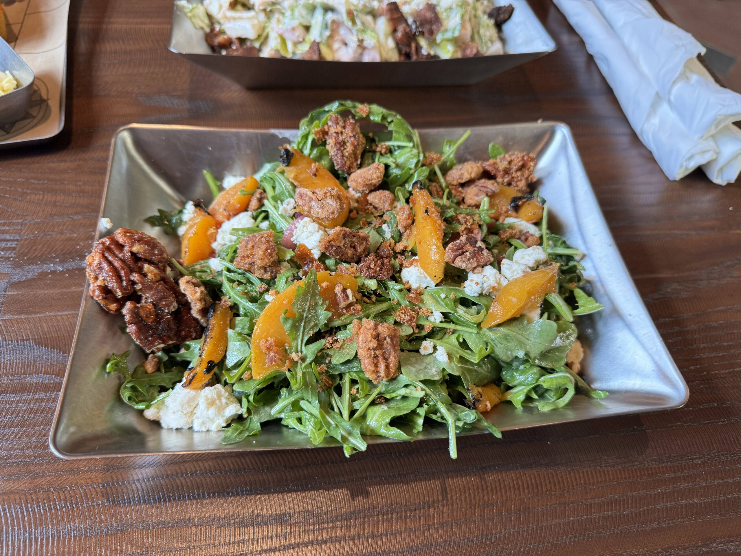 Rectangular plate of salad at The Oak & Star Tavern with greens, candied pecans, peaches, and crumbled cheese.