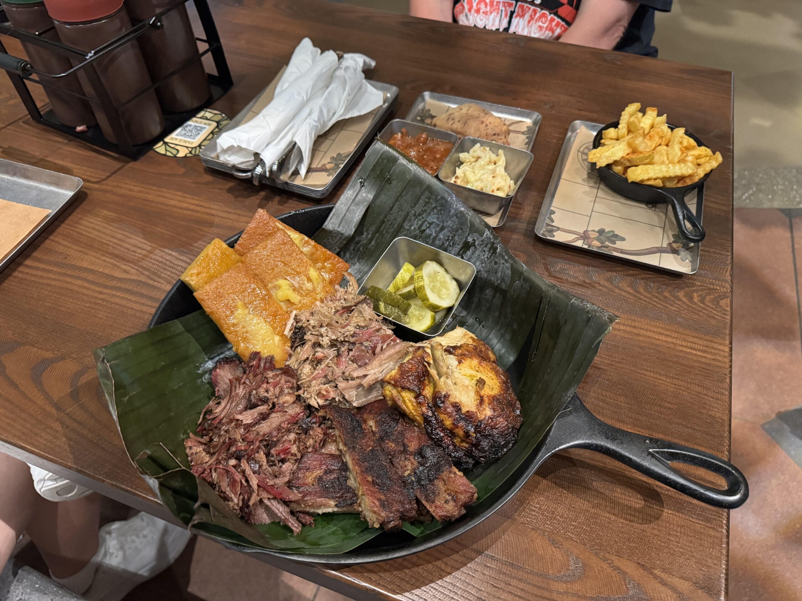 A cast iron pan of barbecue meats and sides at The Oak & Star Tavern, served with cornbread, pickles, and fries.