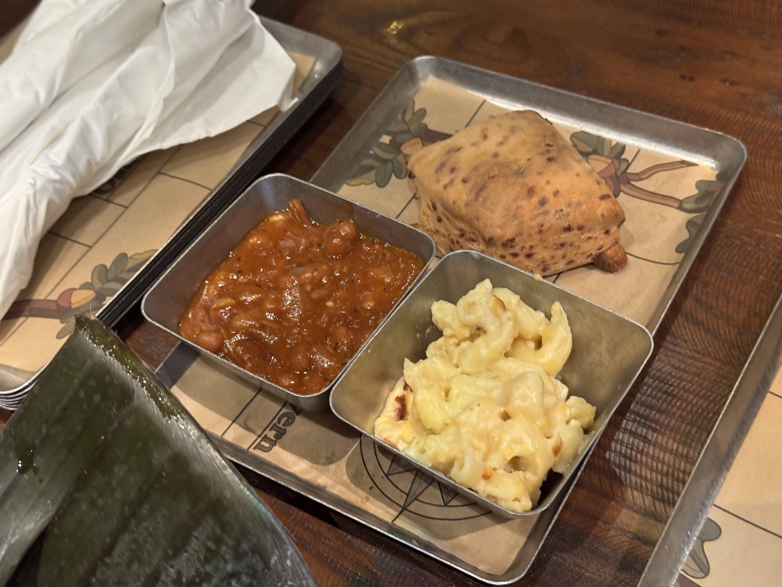 A tray with macaroni and cheese, stew, and a bread roll at The Oak & Star Tavern, set on a wooden table with napkins.