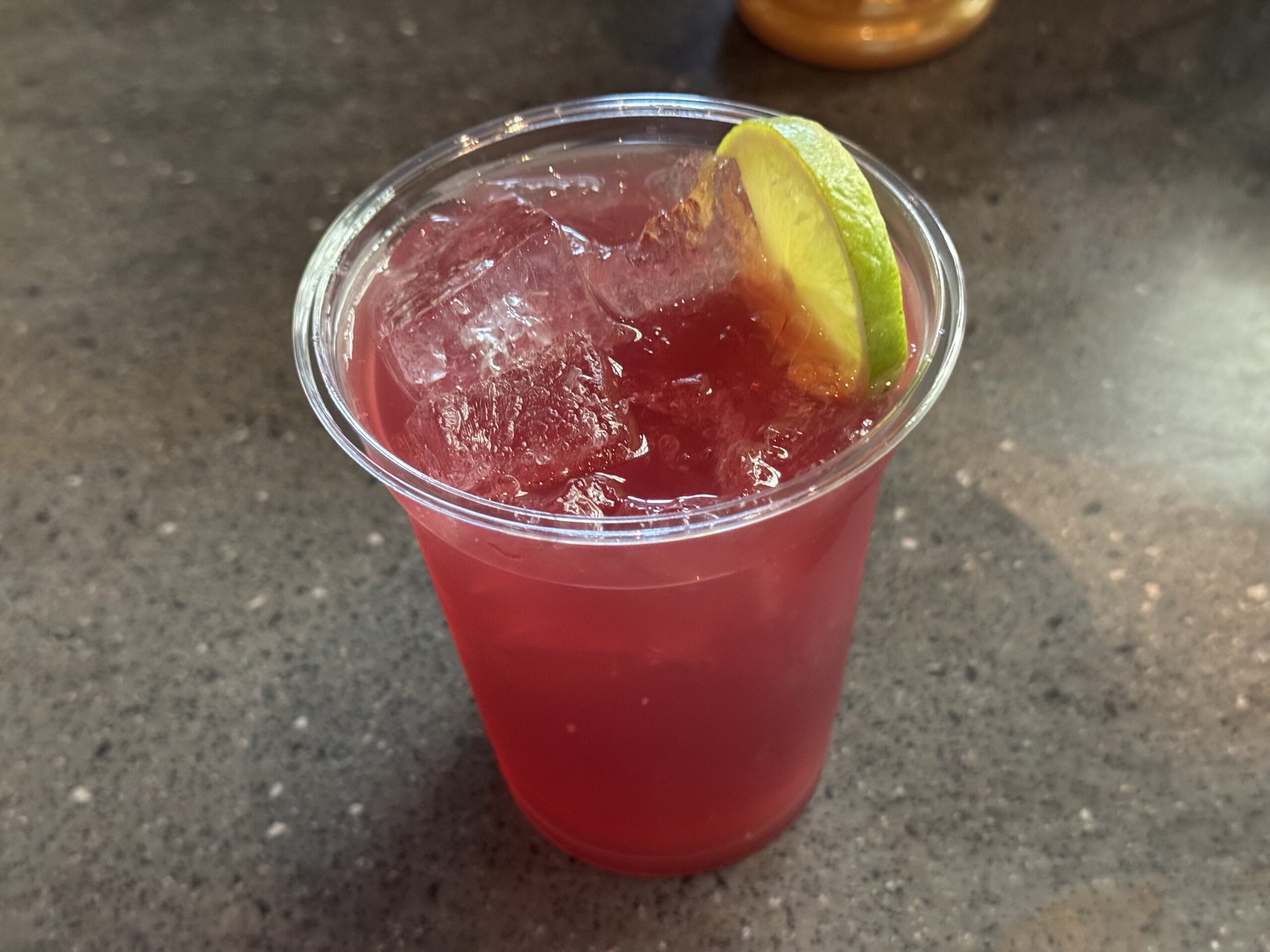 A plastic cup of red iced drink from The Oak & Star Tavern, garnished with lime, on a dark countertop.