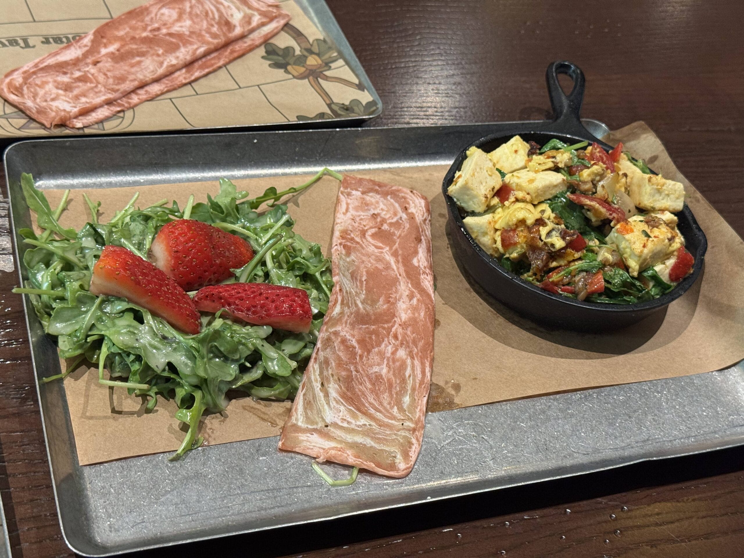 A tray at The Oak & Star Tavern with arugula, strawberries, cured meat, and a skillet of veggie scrambled eggs.