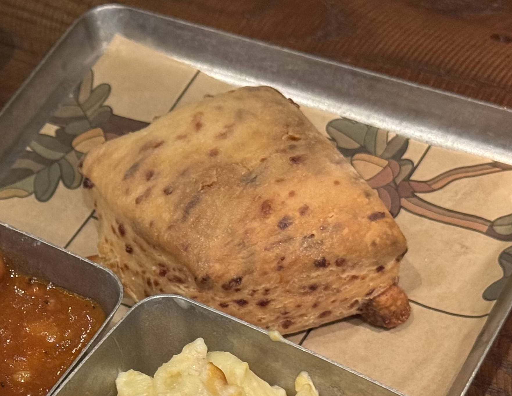 A triangular, baked pastry from The Oak & Star Tavern, served on a metal tray with sauce and pasta.