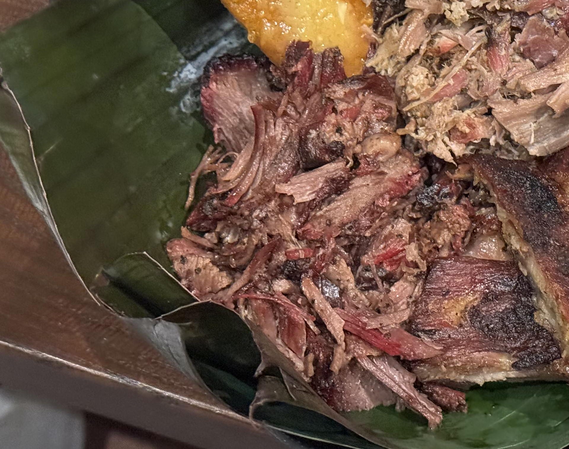 Shredded, cooked meat at The Oak & Star Tavern served on a banana leaf with chunks of roasted plantain in the corner.