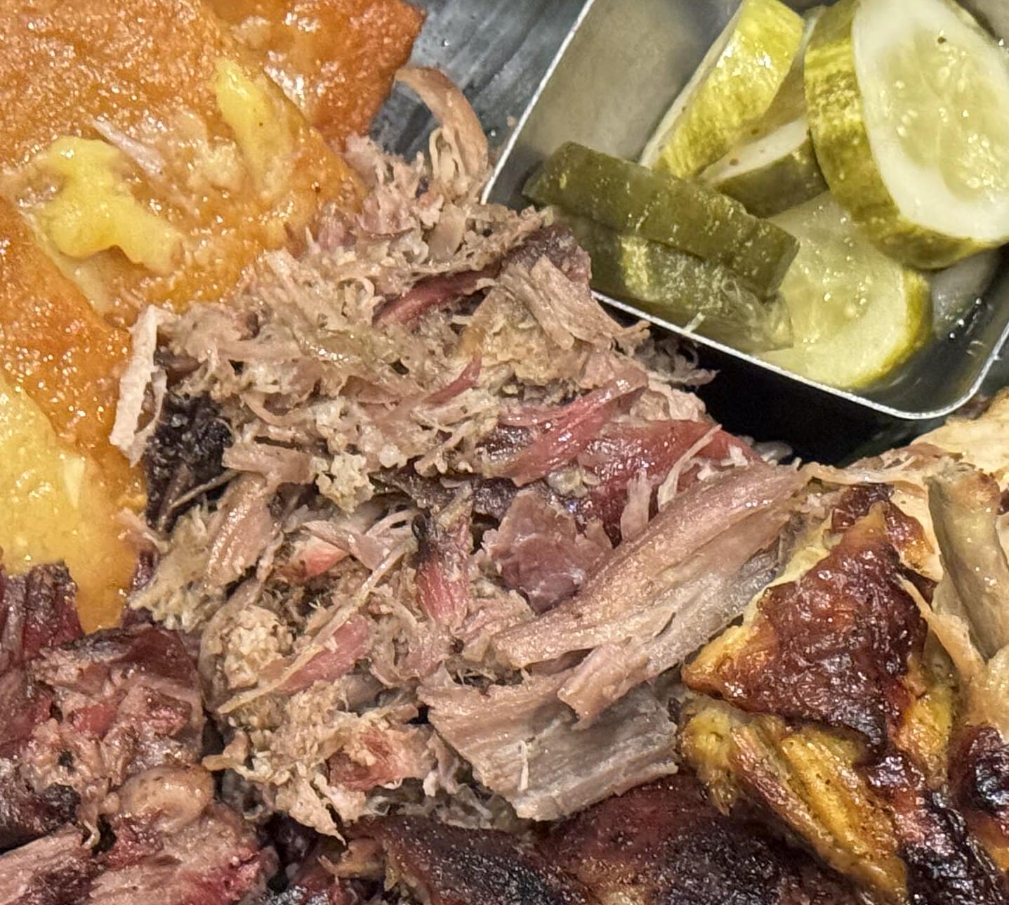 Pulled pork, cornbread, and pickles on a metal tray—a barbecue feast at The Oak & Star Tavern.