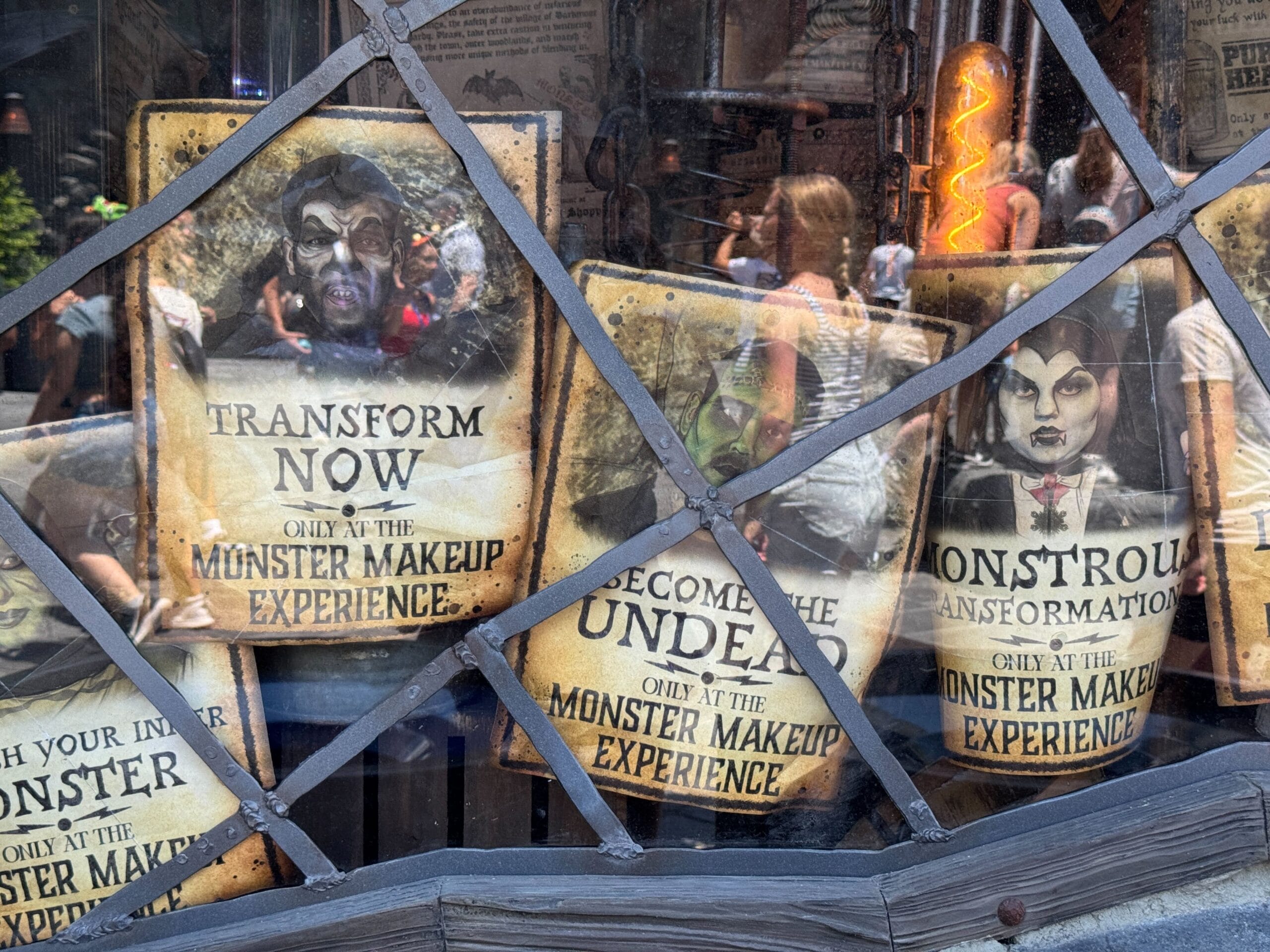 Posters in a window advertise Epic Universe’s Monster Makeup Experience, with spooky faces as people pass by outside.