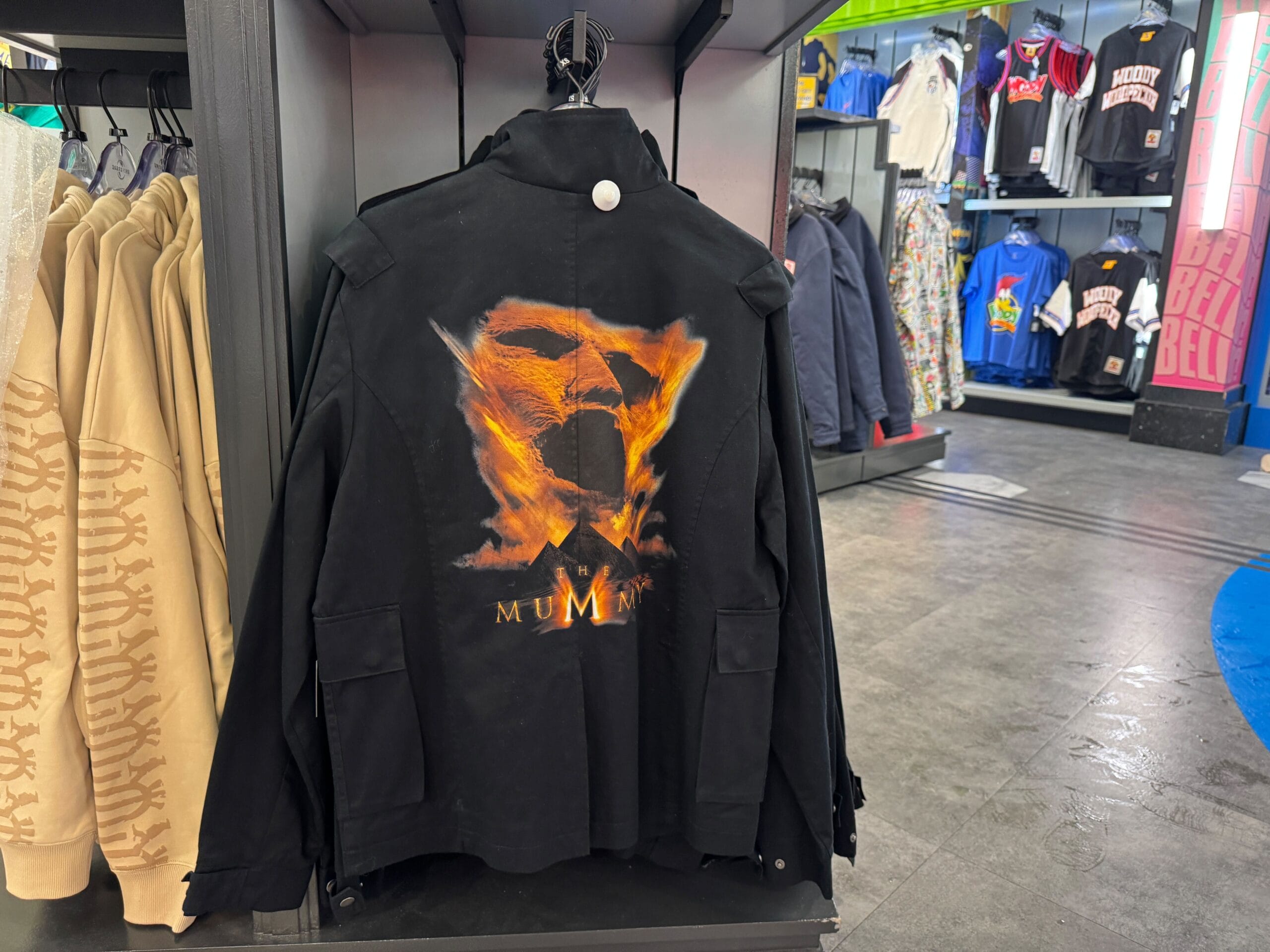 Black jacket from the UNIVRS Mummy Collection featuring "The Mummy" and a fiery face graphic on a retail rack.
