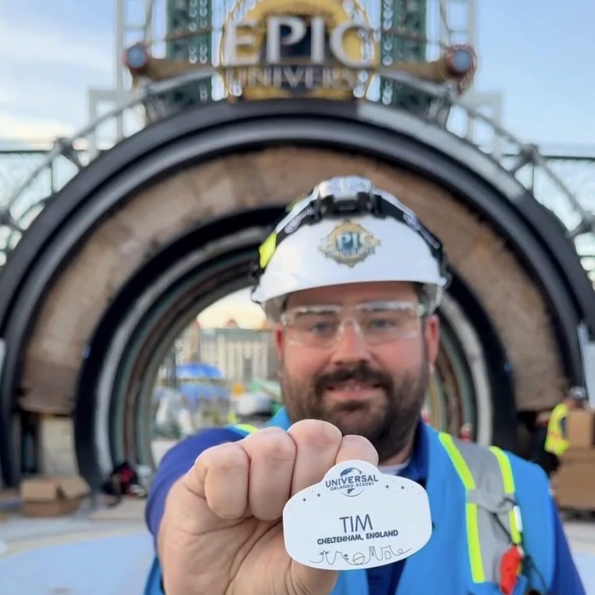 A construction worker with a “Tim” badge stands at Universal Orlando Resort’s Epic Universe entrance, celebrating a wage increase.