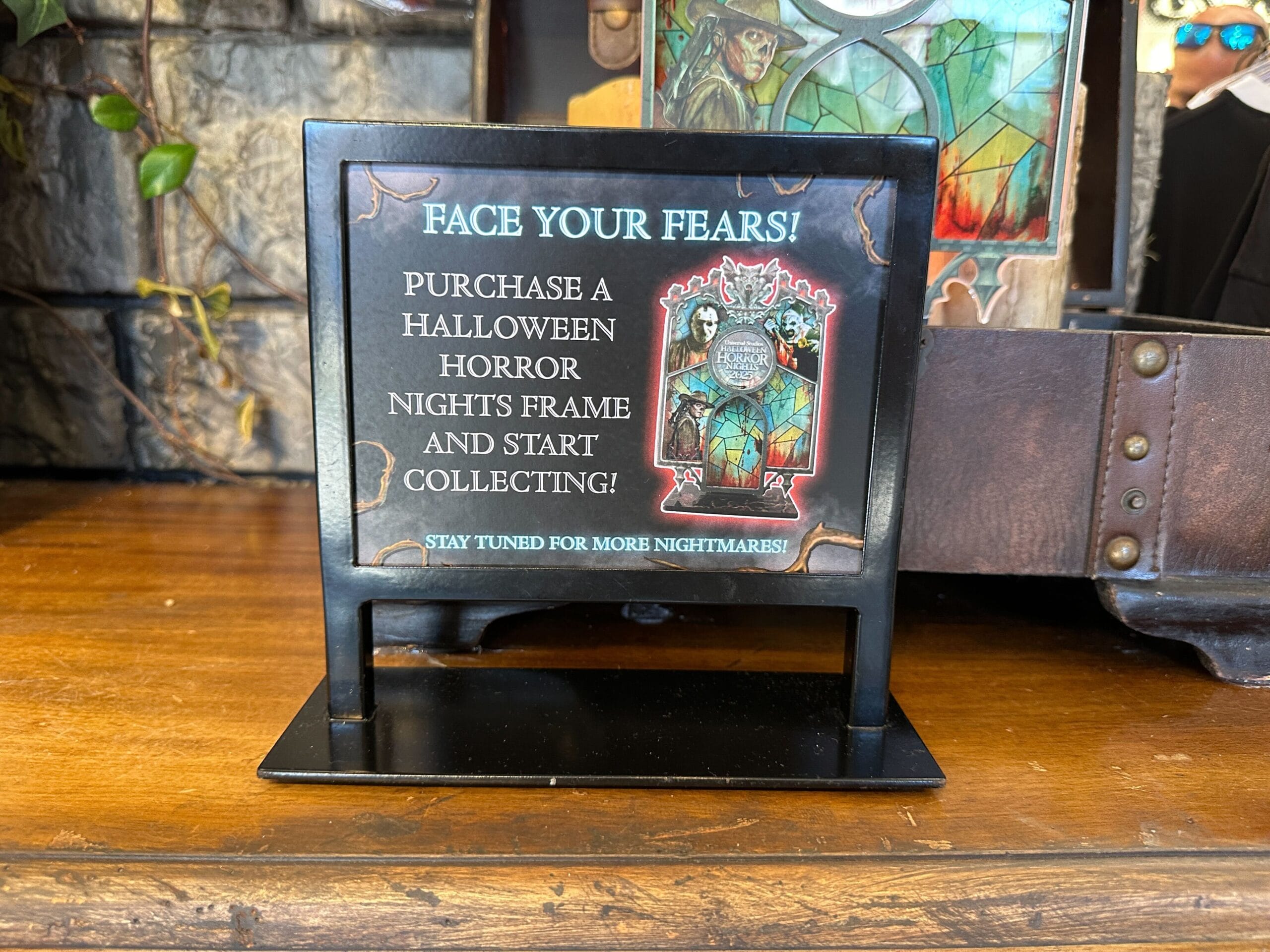 A sign promoting Halloween Horror Nights photo frames sits on a wooden surface near decorative props.