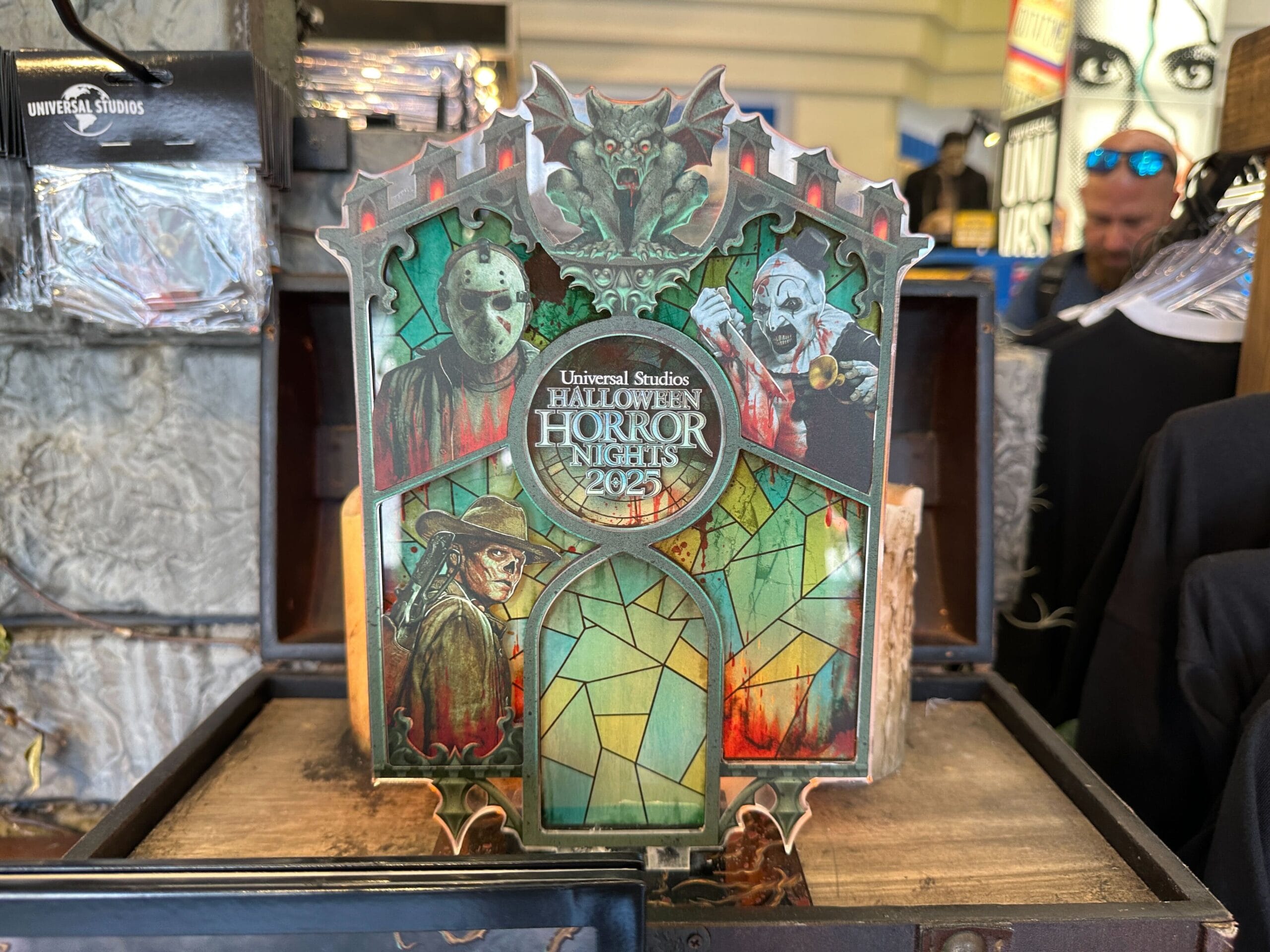 A Halloween Horror Nights 2023 sign with horror villains and stained glass design sits on display in a store.