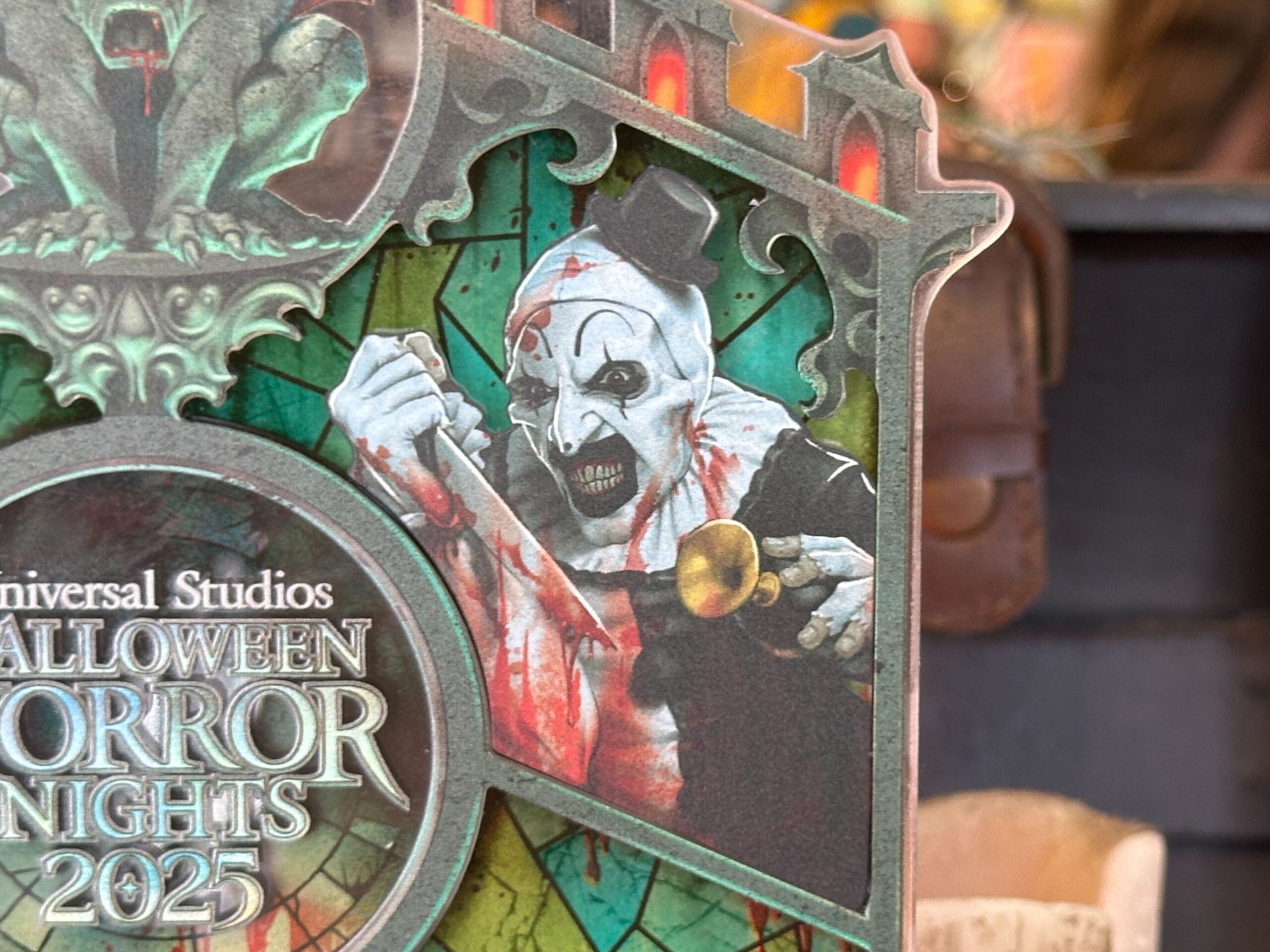A creepy clown with a bloody face and top hat holds a horn on a Halloween Horror Nights 2025 sign.