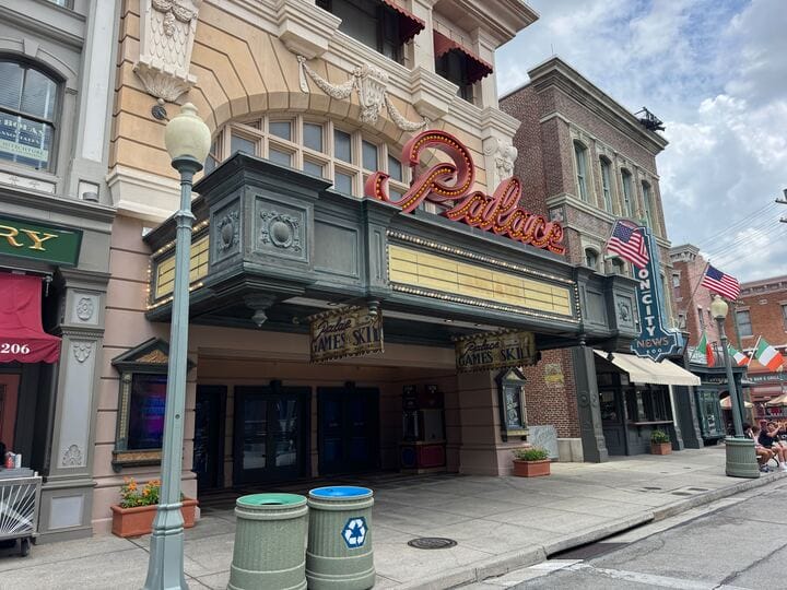 The Palace Theater Arcade with missing letters sign, vintage marquee, shops, and flags on a cloudy day.