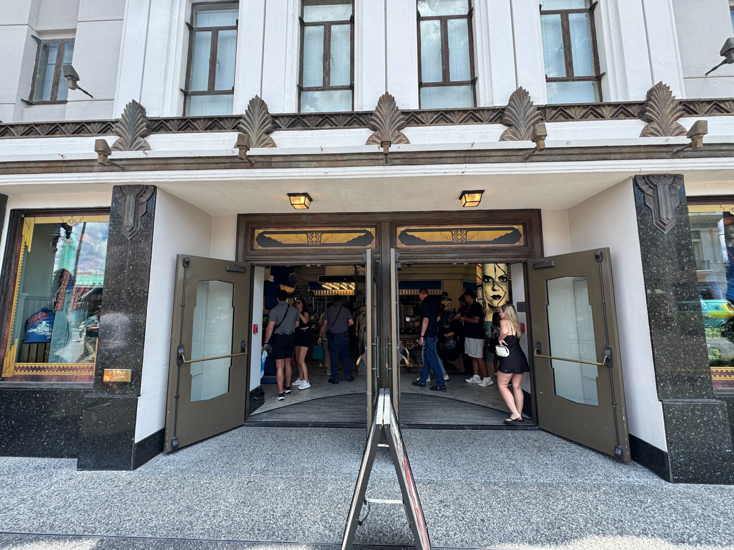 Open double doors of a building with people entering and exiting; art deco details above the entrance.