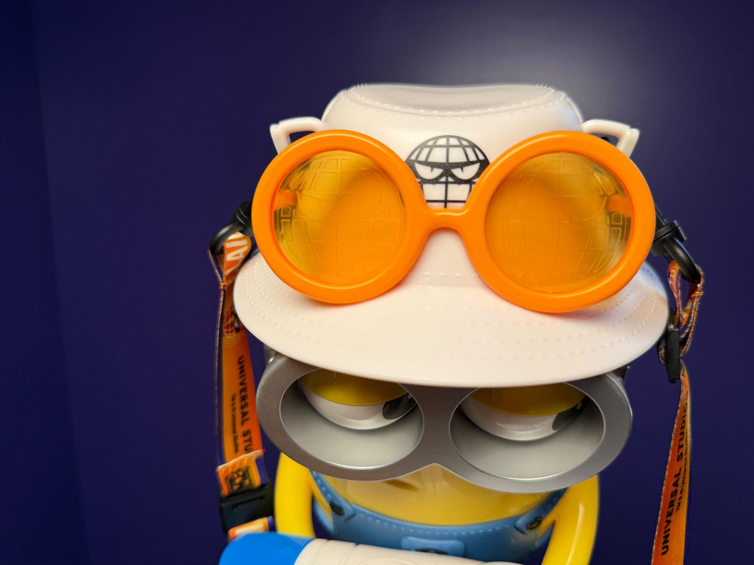 Villain-Con Minion toy with orange goggles, a white hat, and safety straps; Universal Studios Japan exclusive.