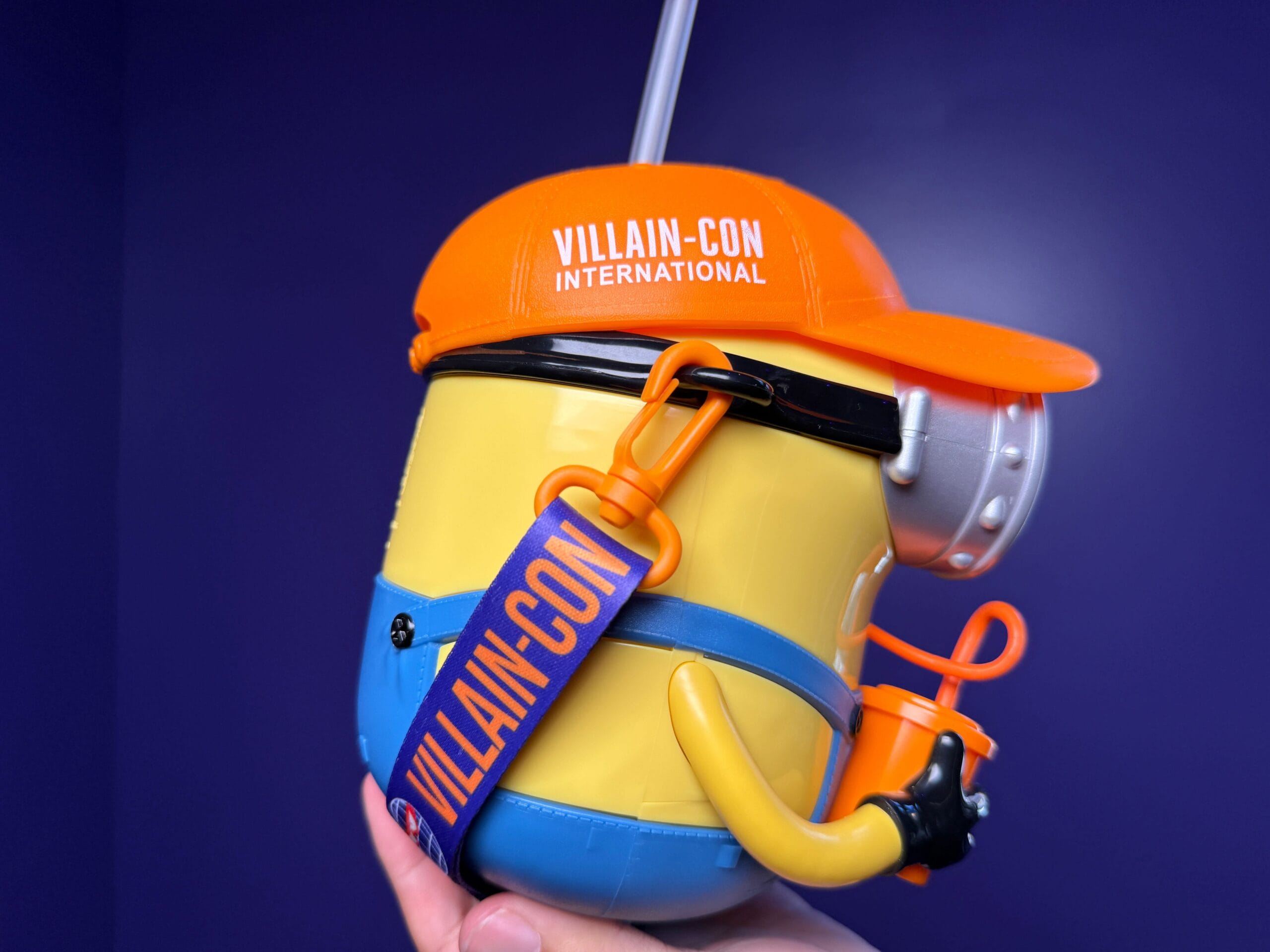 A Minion-shaped drink bottle with a "VILLAIN-CON" hat, held against a purple backdrop at Universal Studios Japan.