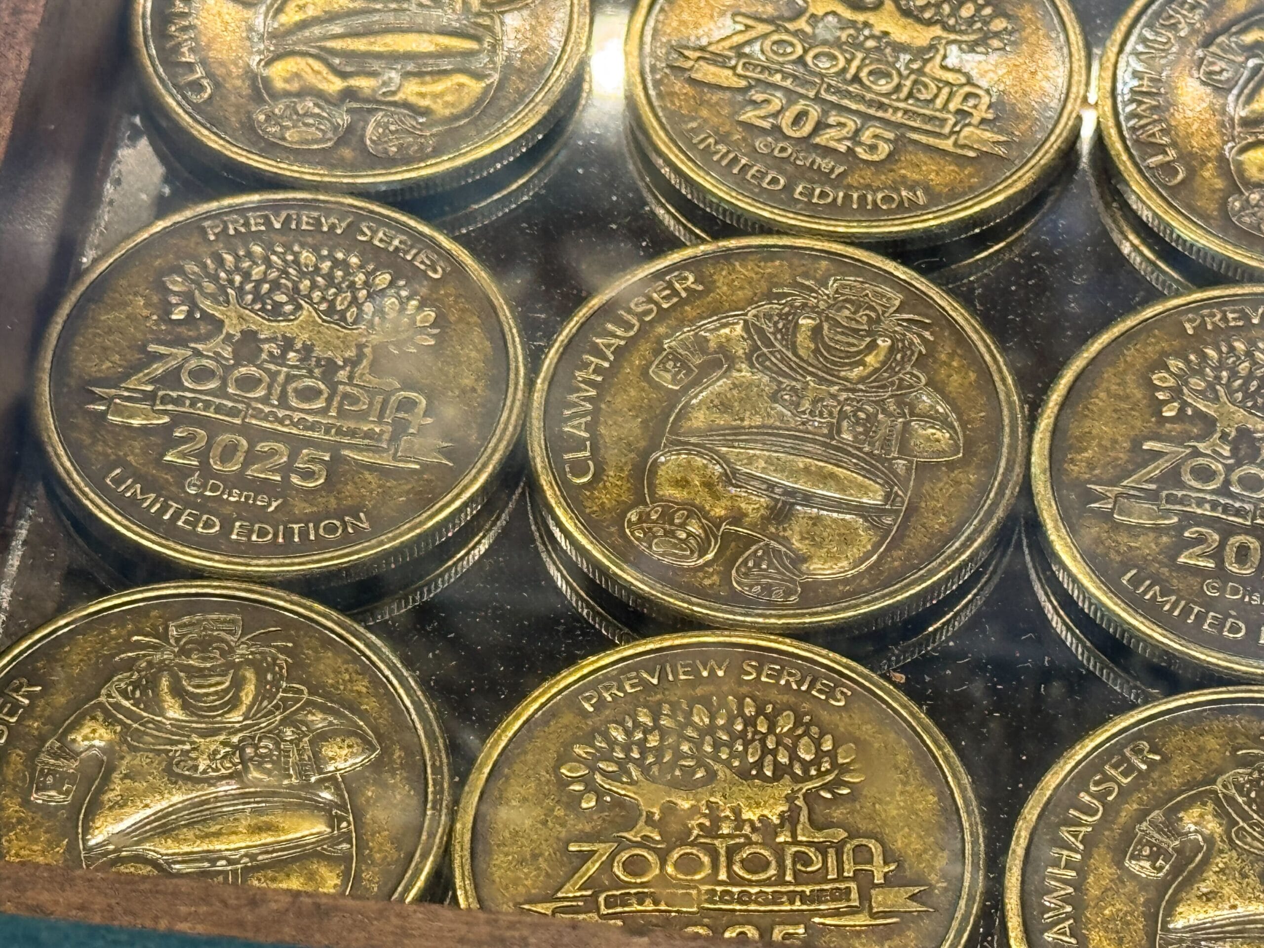 A close-up of collectible medallions: limited edition 2025 Zootopia coins with Clawhauser in a display case.