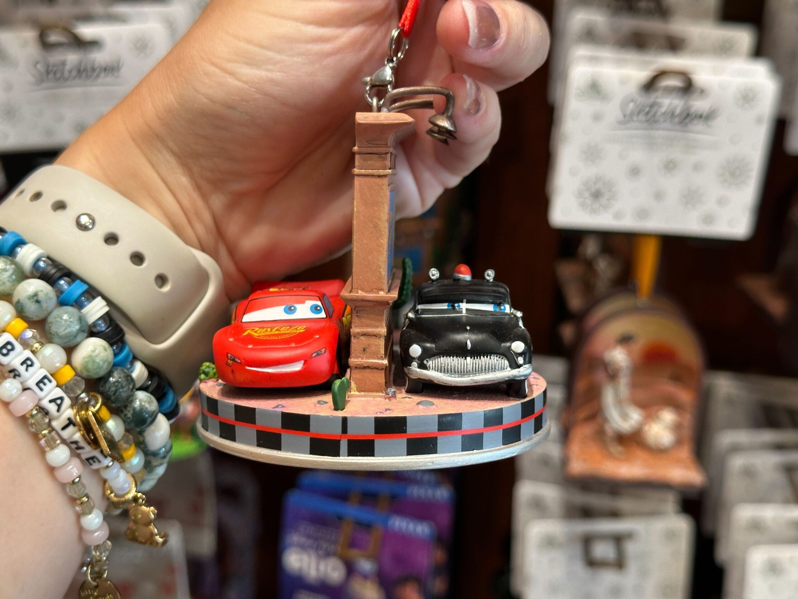 Hand holding a Cars-themed ornament with Lightning McQueen and Doc Hudson on a round base.