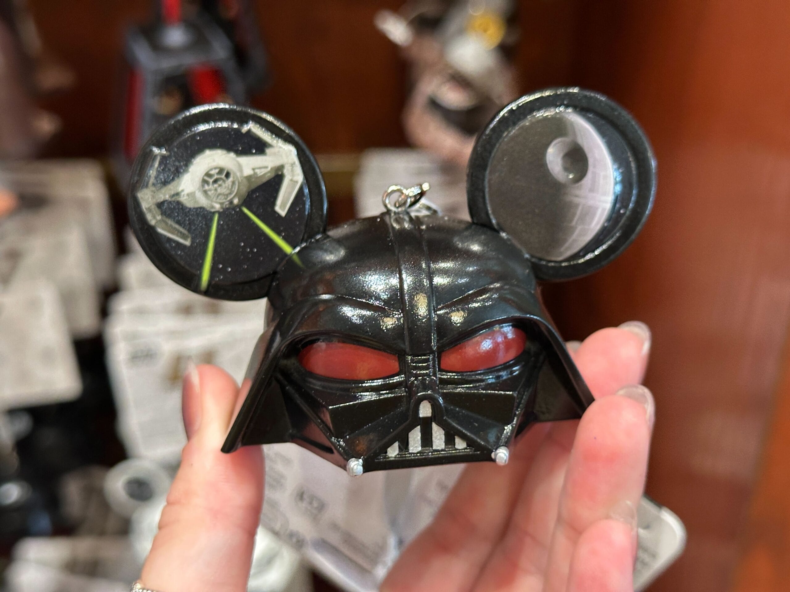 A hand holds a Darth Vader ornament with Mickey Mouse ears, featuring a TIE fighter and Death Star on the ears.