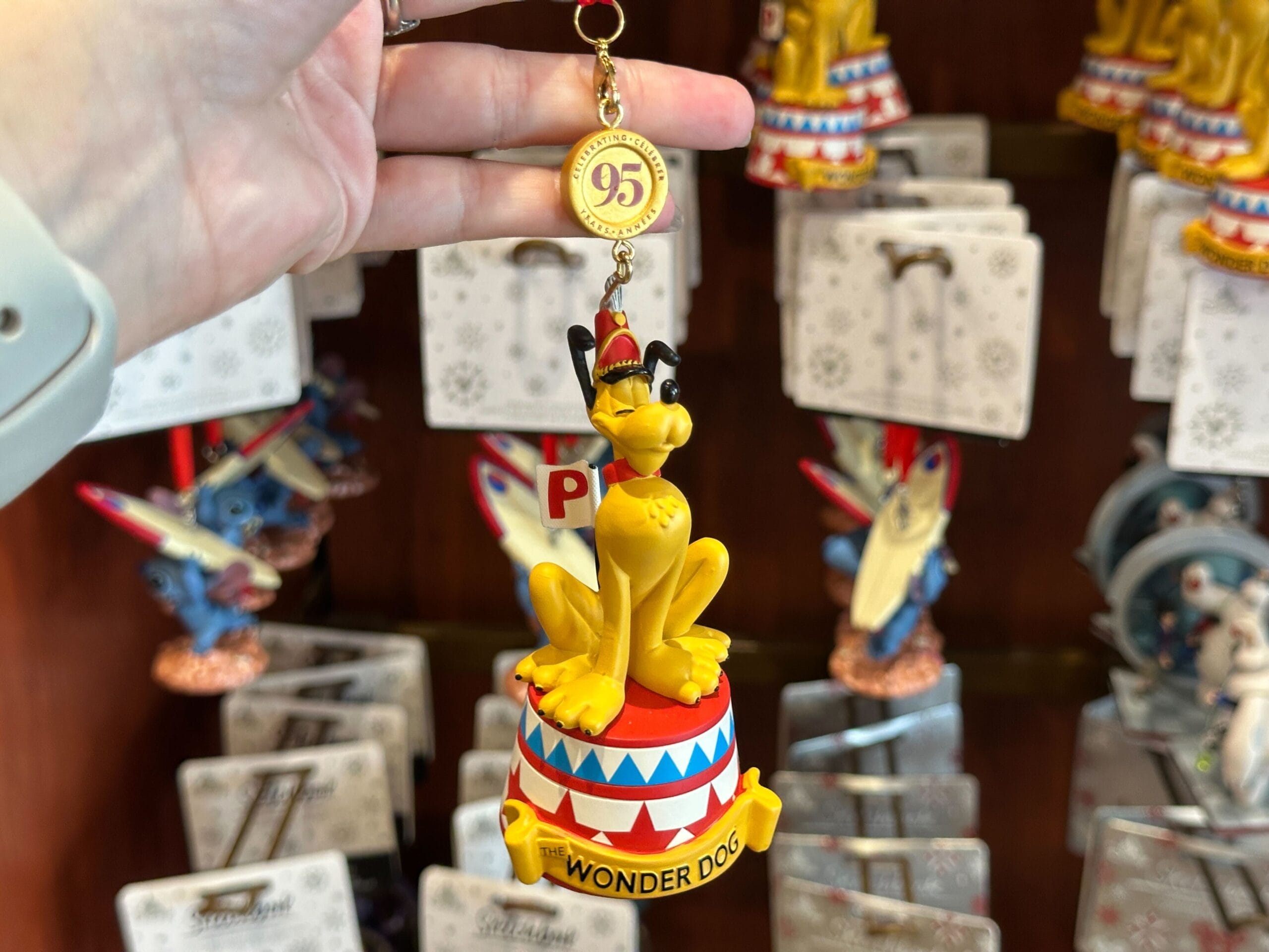 A hand holds a Pluto "Wonder Dog" ornament with a 95th anniversary tag in a shop display.