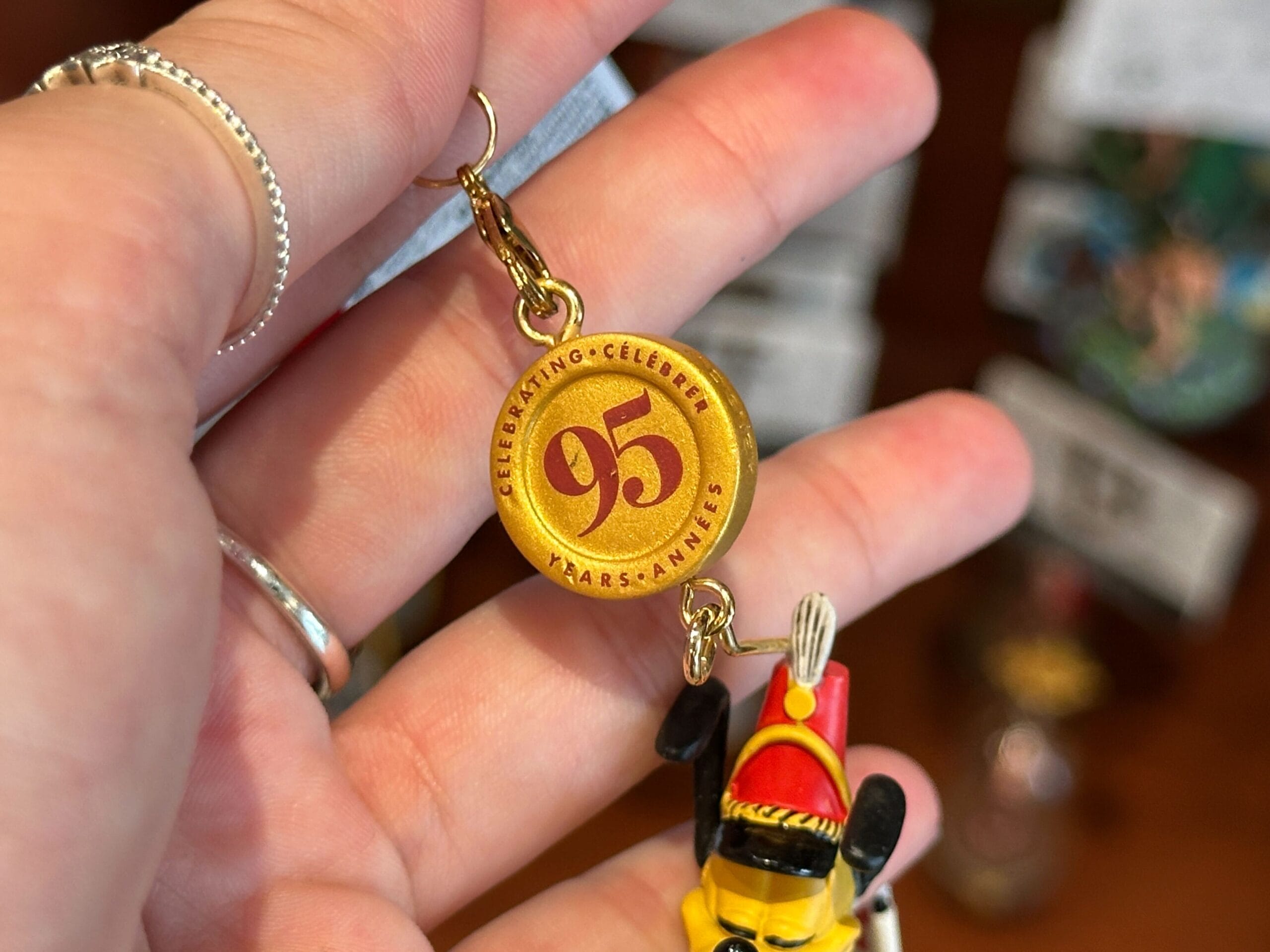 A hand holds a gold Disney keychain charm that reads "Celebrating 95 Years" in red text.