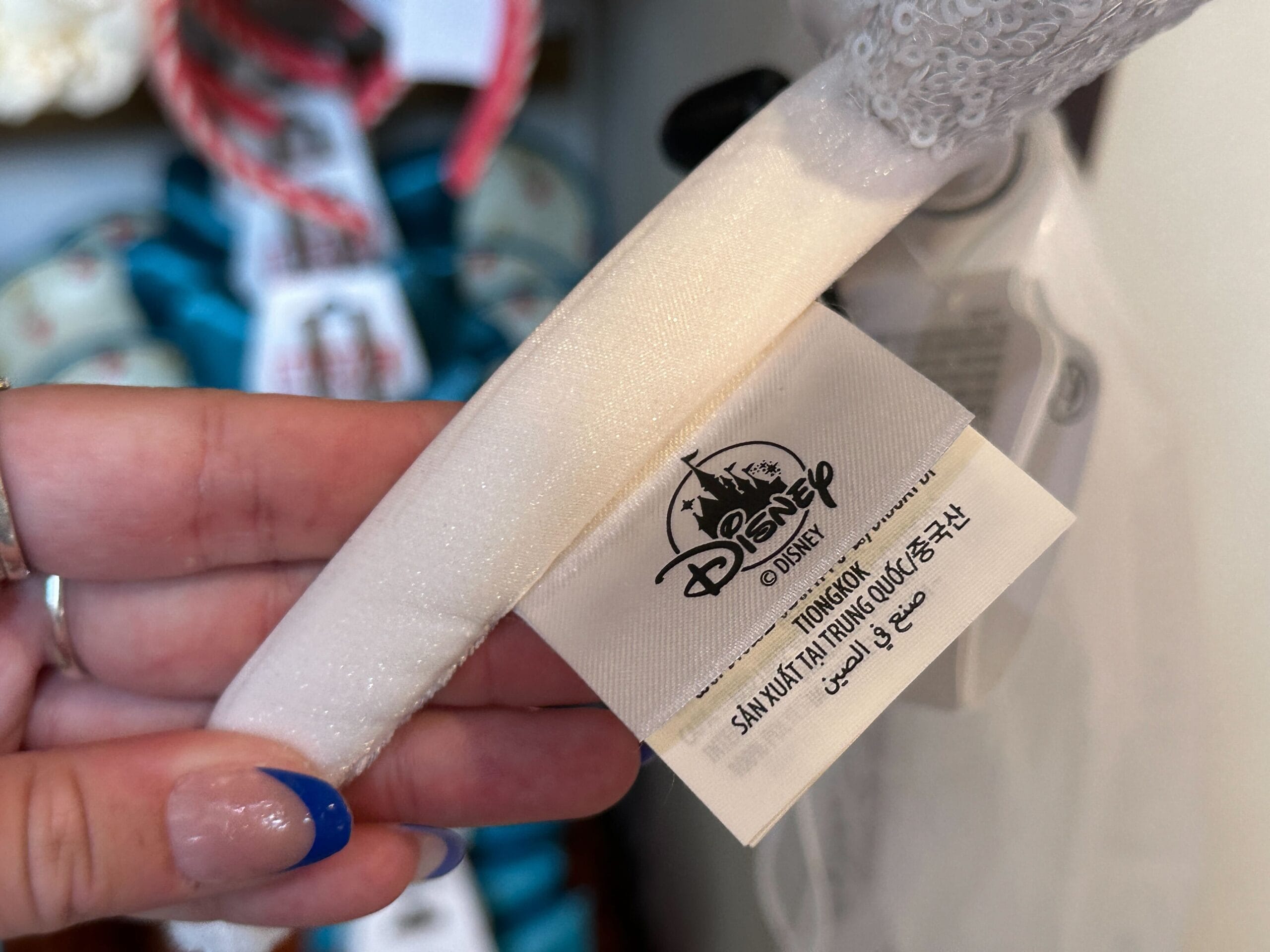 A hand holds a Disney tag attached to a white fabric item, with text in multiple languages.