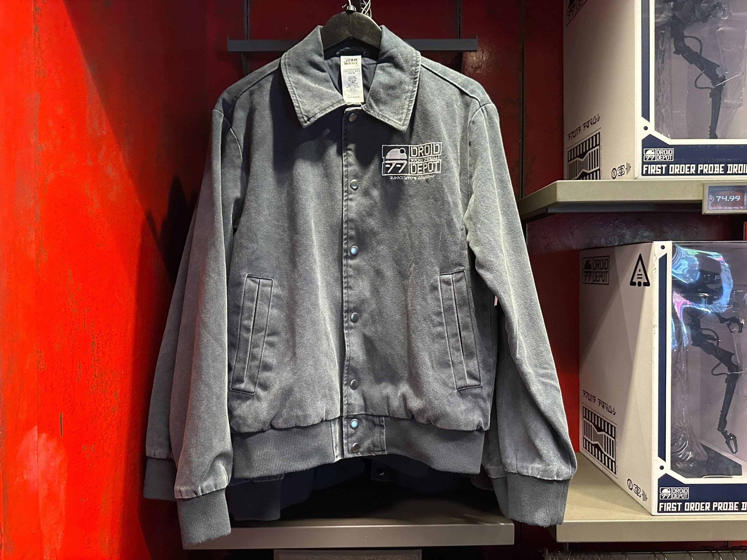 A Droid Depot Jacket hangs on a rack beside Star Wars-themed merchandise boxes.