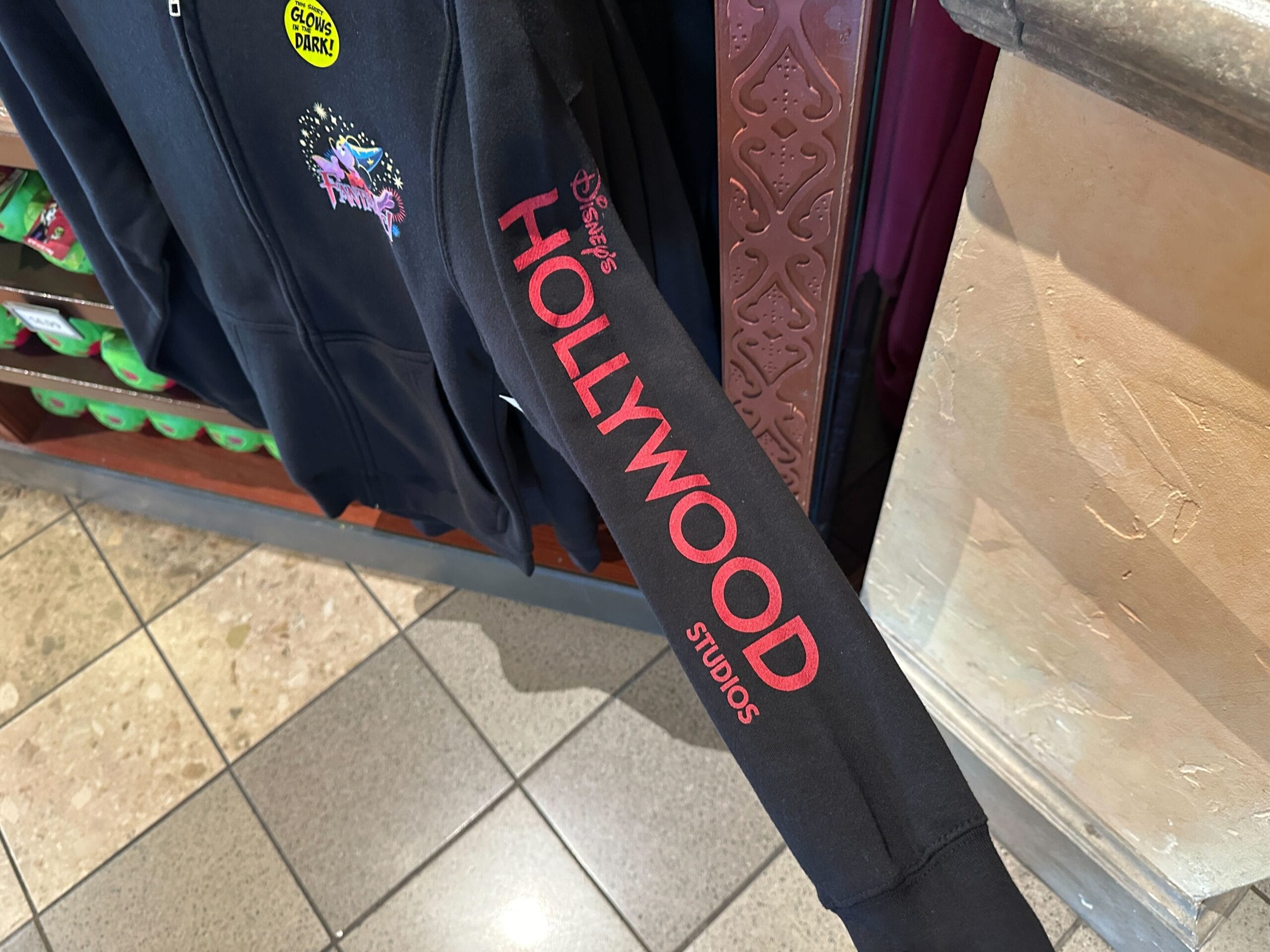 A black sleeve with "Disney's HOLLYWOOD STUDIOS" in red text, shown inside a store with tile flooring.
