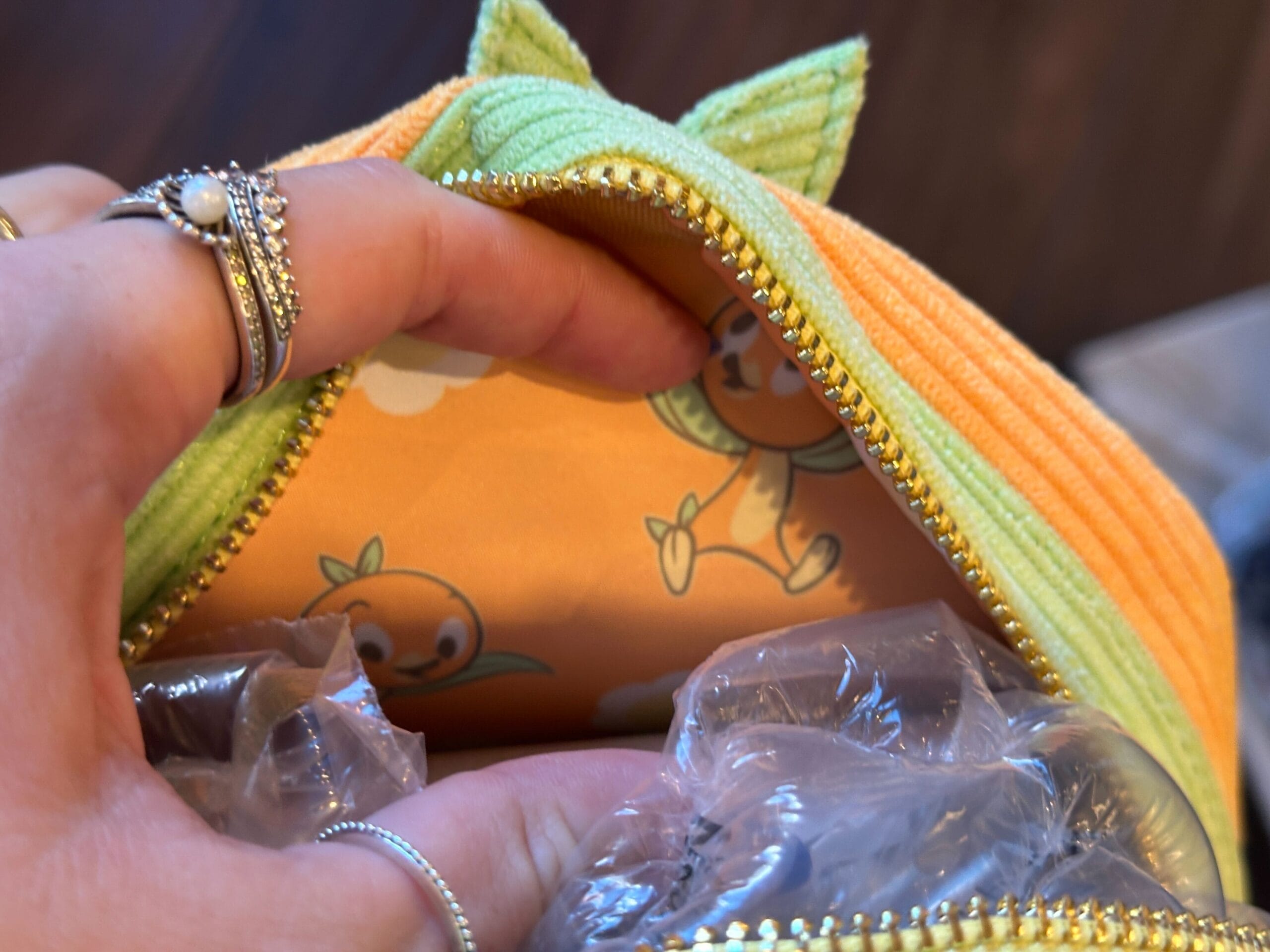 A hand opens an orange zip pouch from Loungefly, revealing an Orange Bird cartoon character on the inner lining.