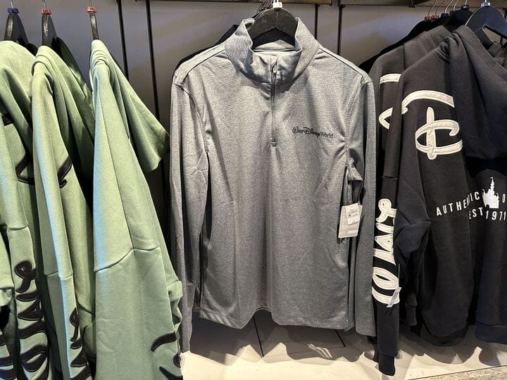 Gray Walt Disney World pullover displayed among green and black apparel in a clothing store at Hollywood Studios.