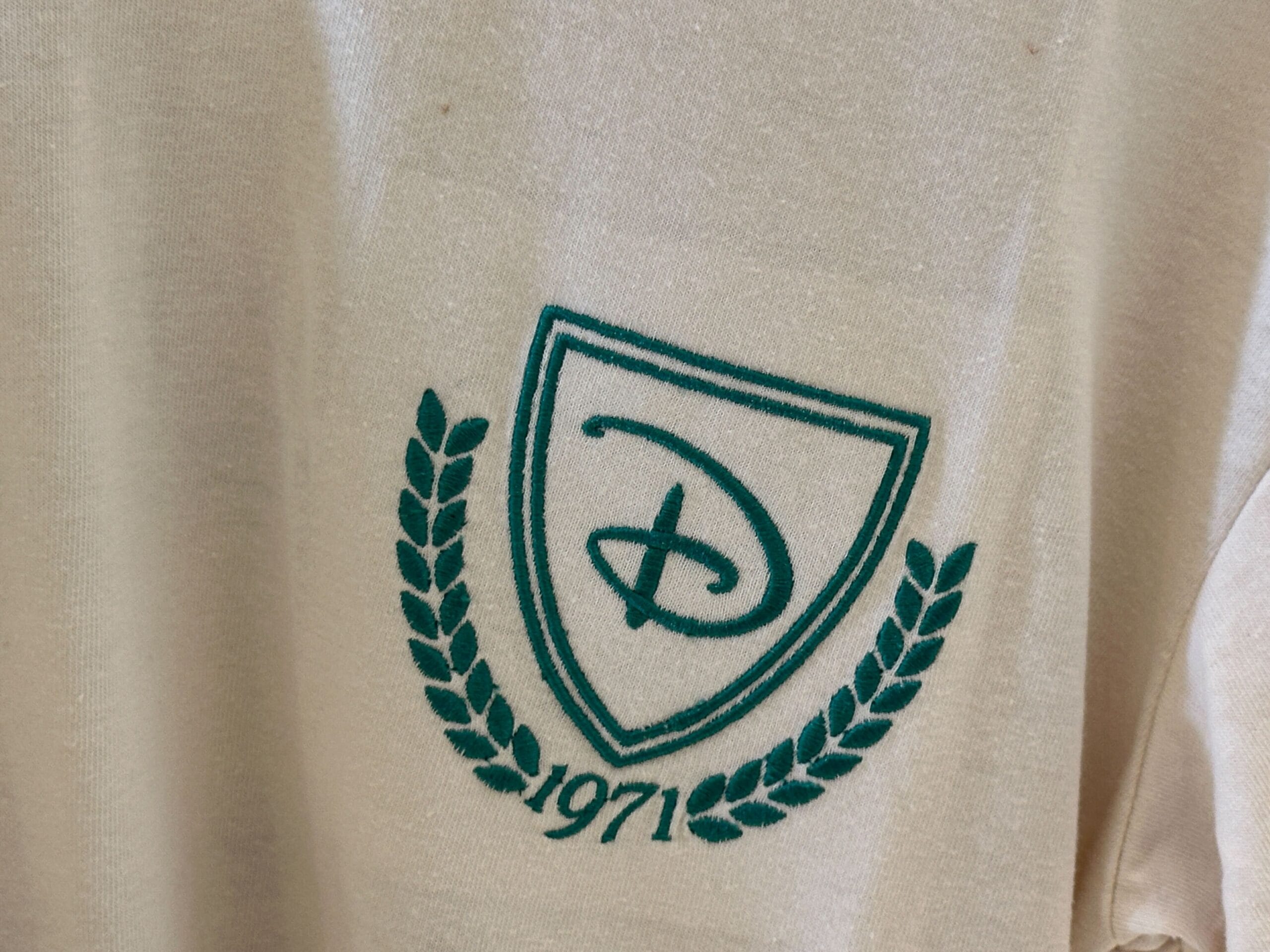 Cream-colored apparel featuring a green shield logo, laurel branches, "1971," and Walt Disney World-inspired details.