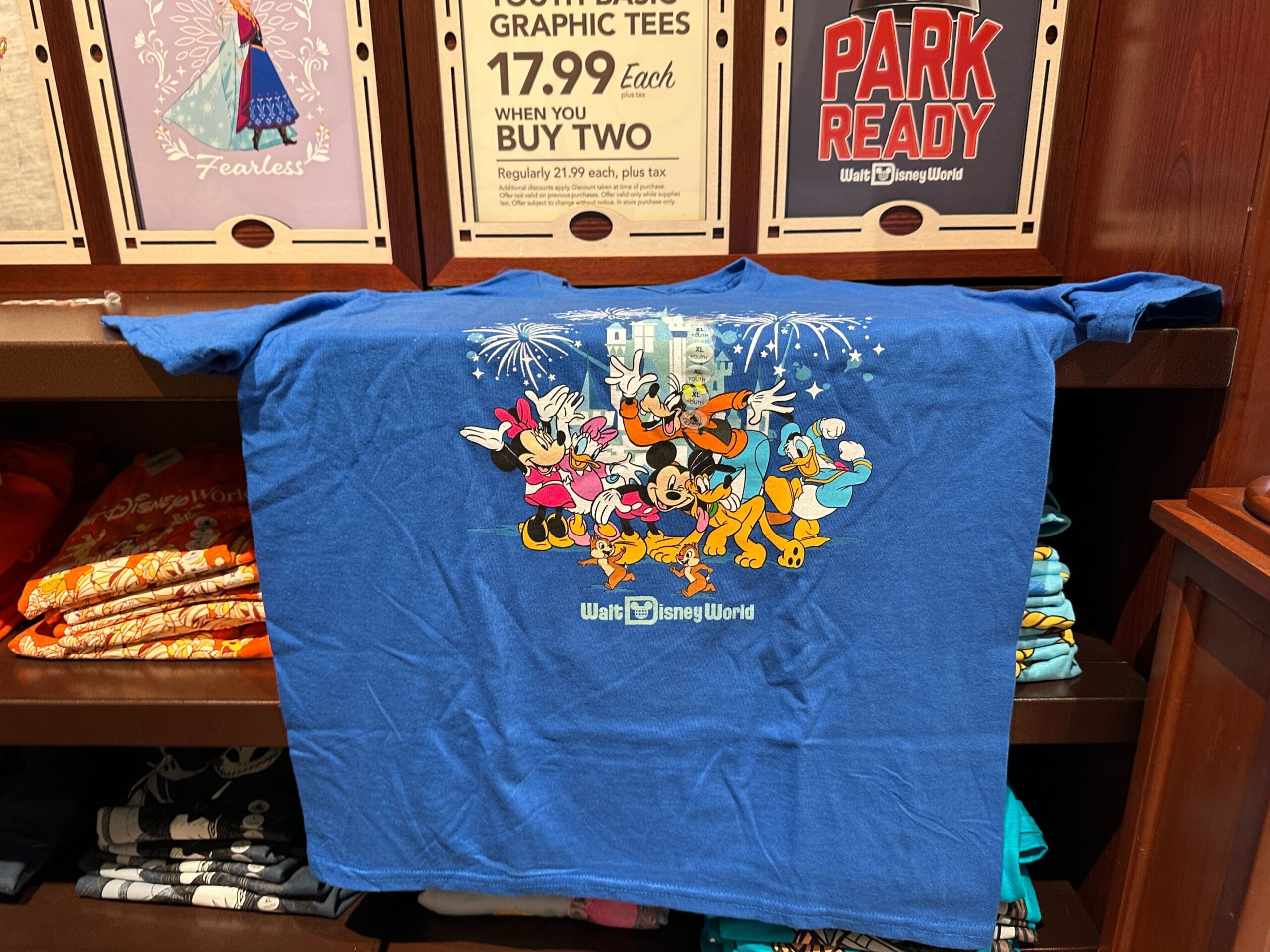 Blue Walt Disney World apparel t-shirt featuring Minnie, Daisy, Goofy, Mickey, Pluto, and Donald in front of fireworks and the castle.