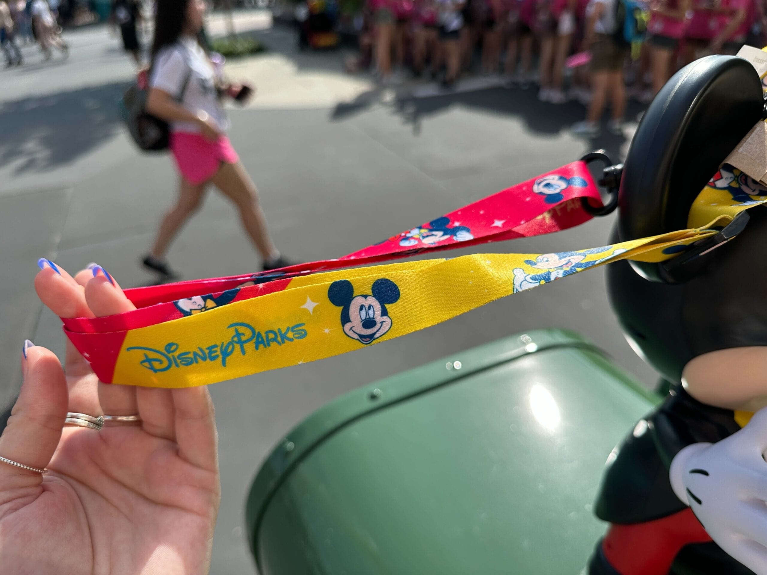 Hand holding a colorful Disney Parks lanyard with Mickey Mouse designs, near the talking Mickey Mouse popcorn bucket at hollywood studios