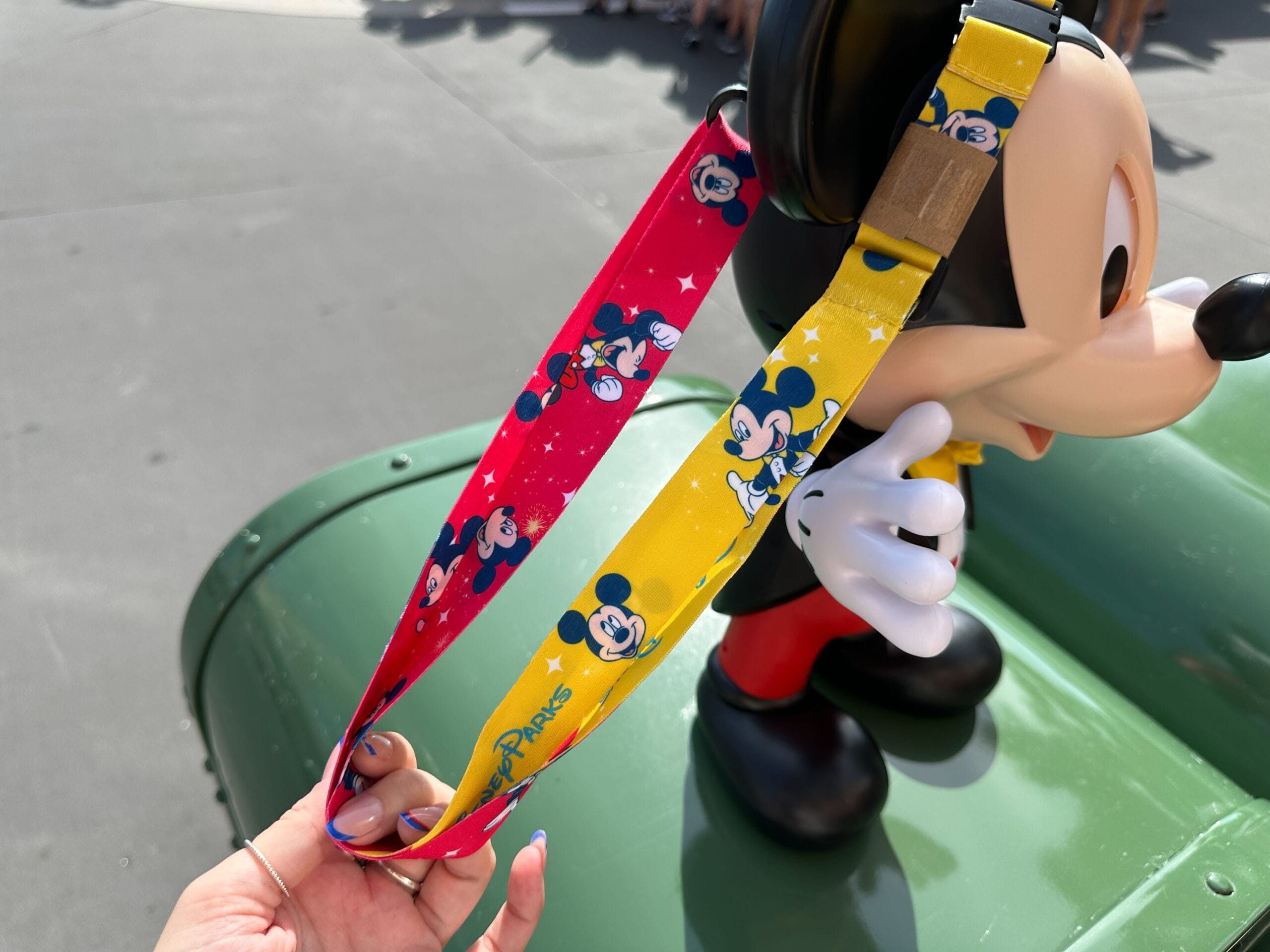 A hand holds a colorful Mickey Mouse lanyard near a talking mickey popcorn bucket at hollywood studios
