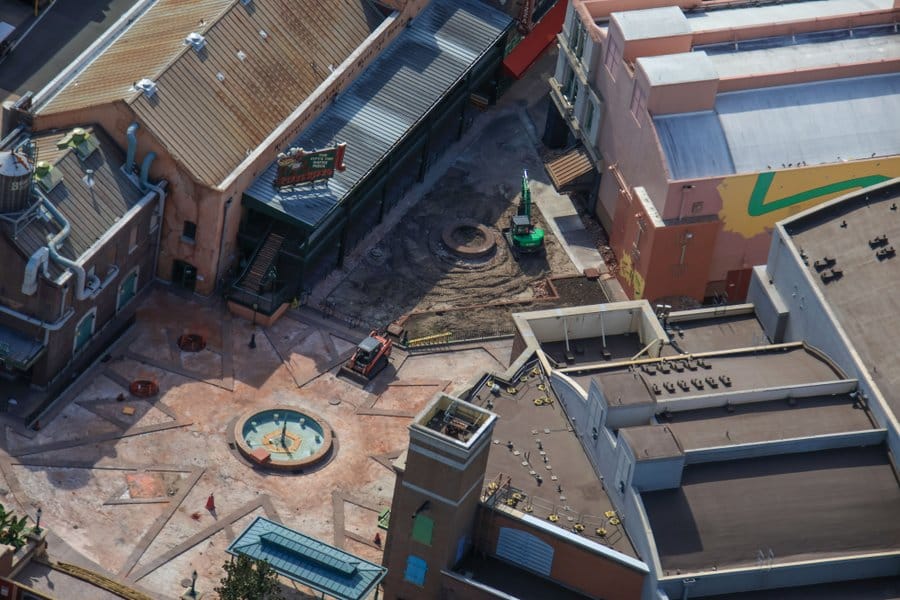 Aerial photo of early work: plaza with construction vehicles, bare ground, and buildings around a small circular fountain.