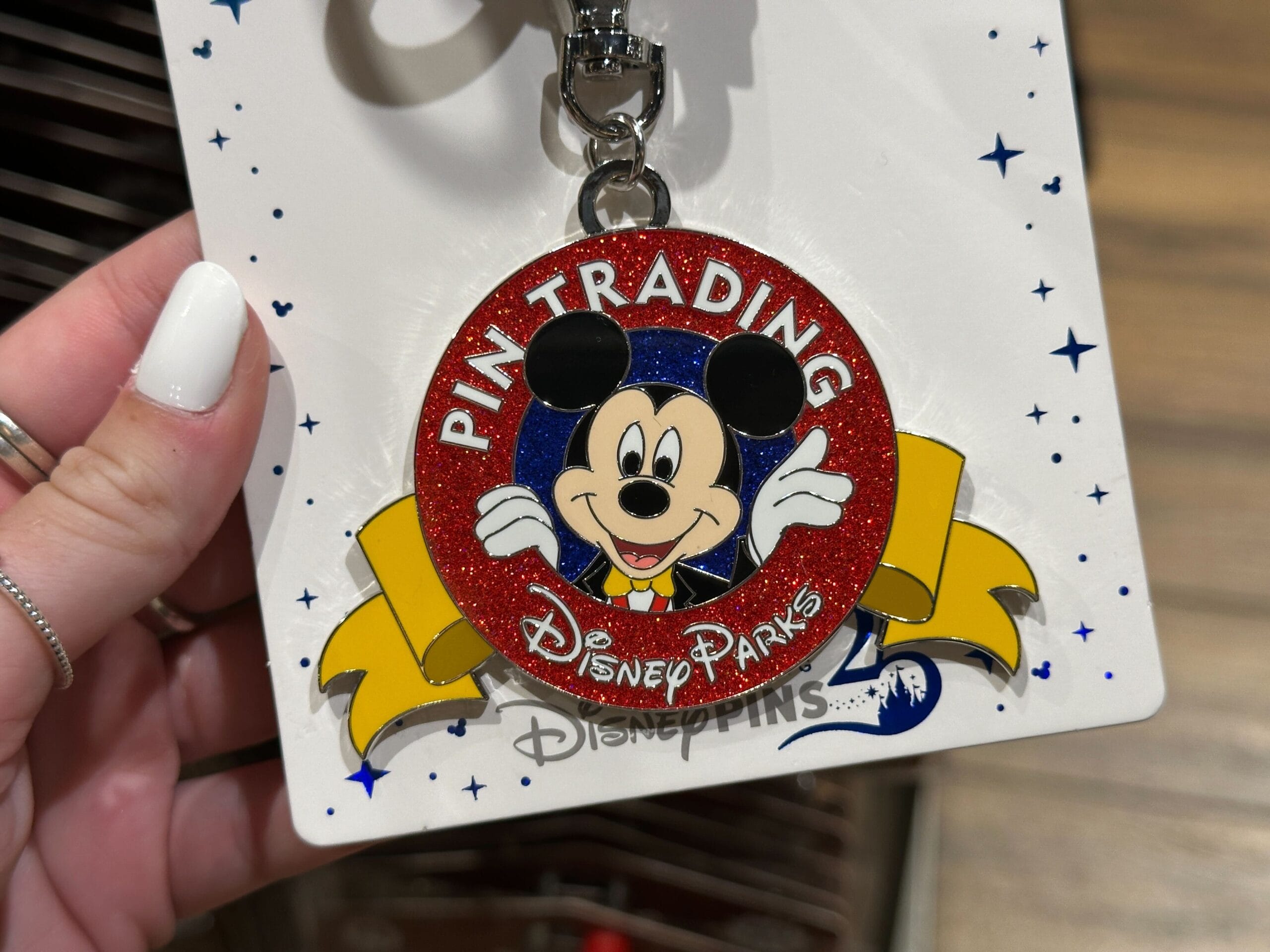 Hand holding a Disney Parks pin featuring Mickey Mouse with "Pin Trading" written in a red circle.