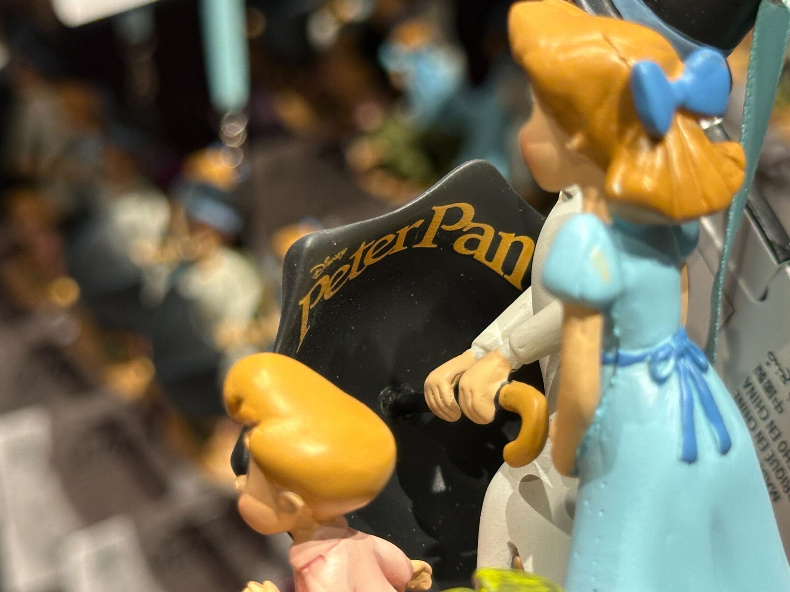 Close-up of Peter Pan figurines featuring Wendy and a child in blue, with a 'Peter Pan' sign in the background.