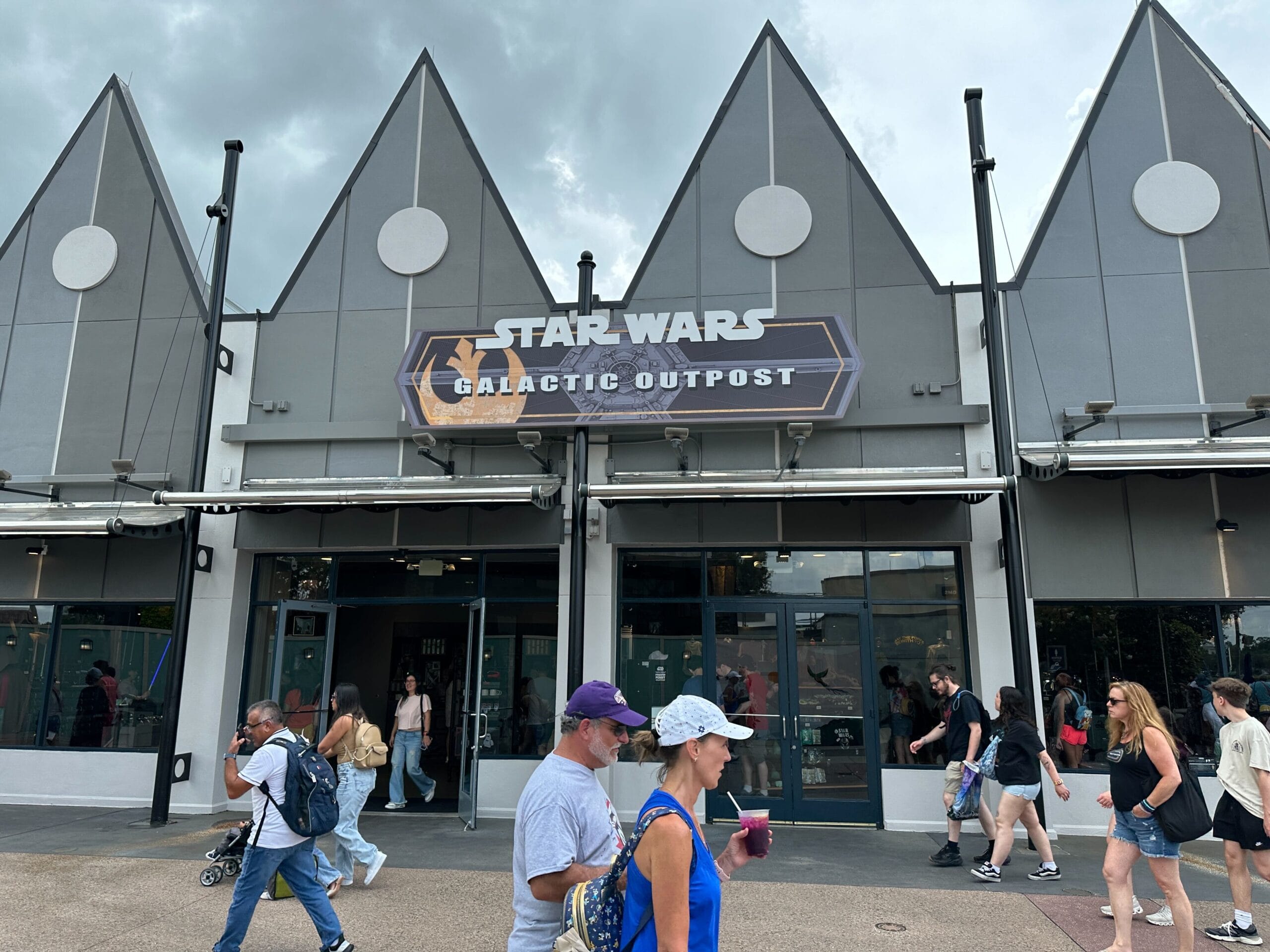 People walk past the Star Wars: Galactic Outpost store, browsing Droid Depot Pins under a cloudy sky.