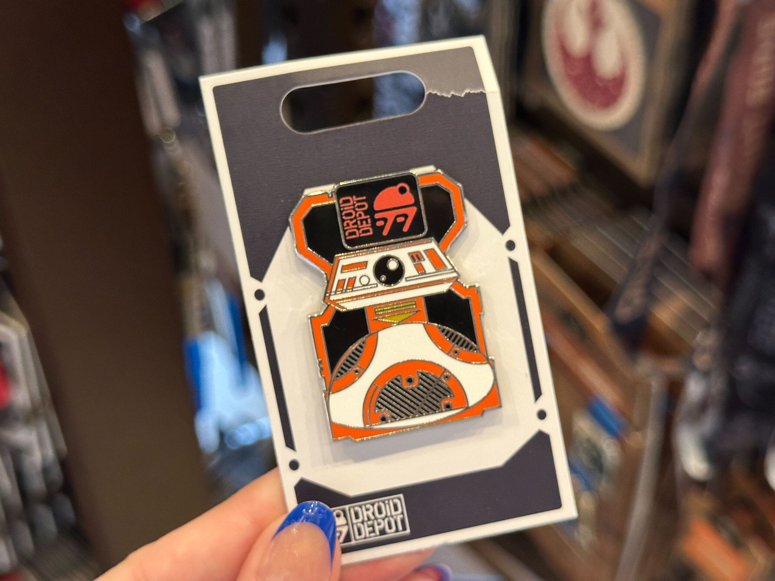 A hand holds a Droid Depot BB-8 enamel pin, a must-have Star Wars collectible from the Droid Depot pins collection.