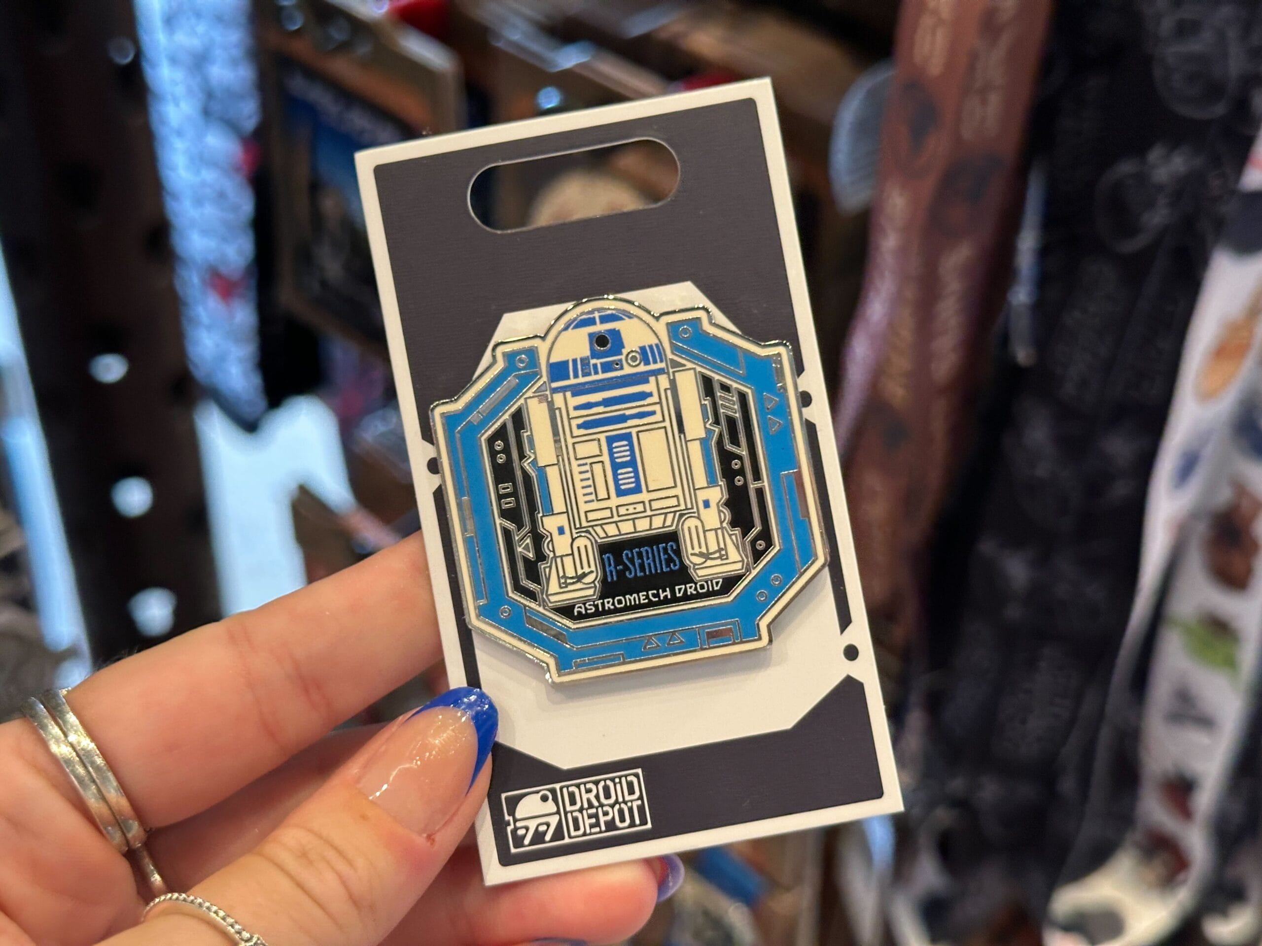 Hand holding a Droid Depot Pin featuring an R-Series Astromech Droid on a branded card in-store.