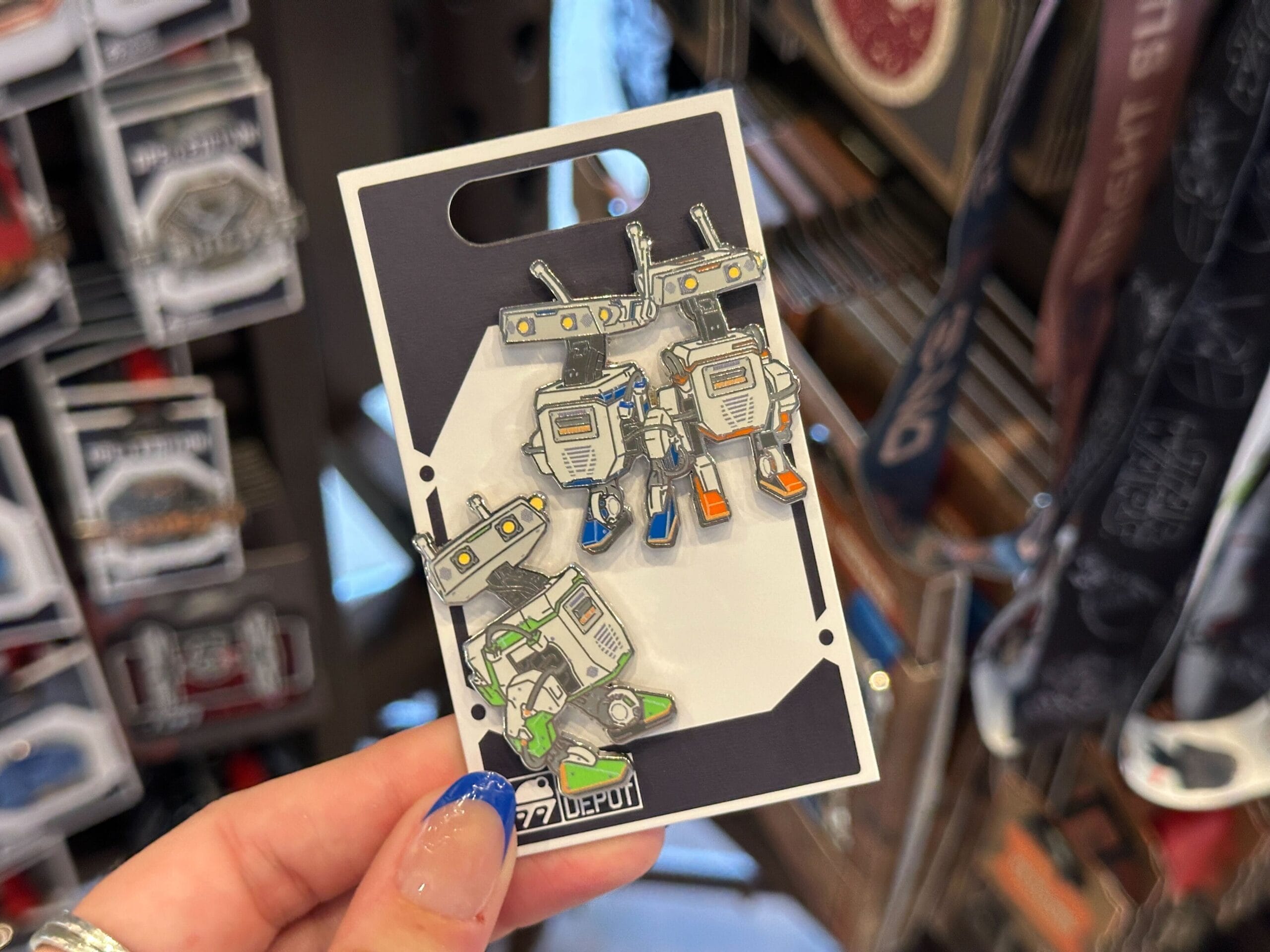 A hand holds a card with three themed Droid Depot Pins in a Star Wars store display.