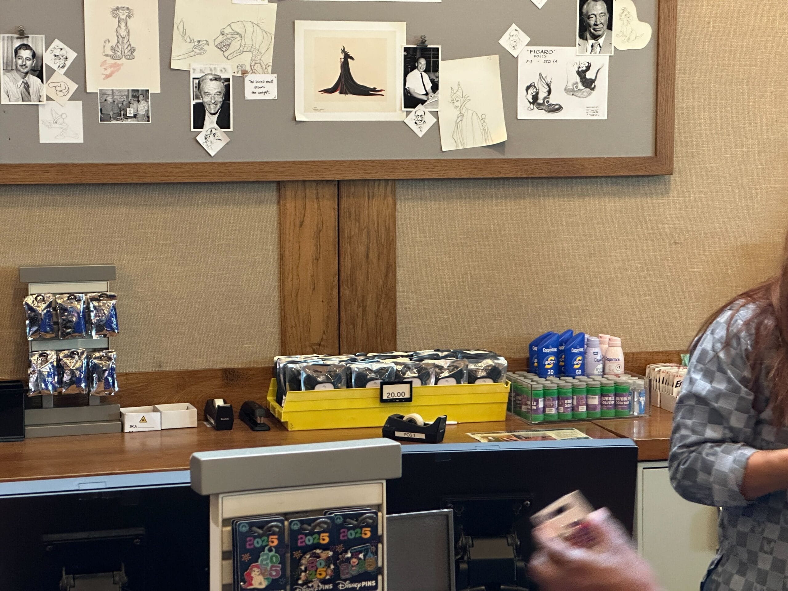A wall with sketches and photos above a counter displaying snacks, mints, Touchland Hand Sanitizer, and Disney card packs.