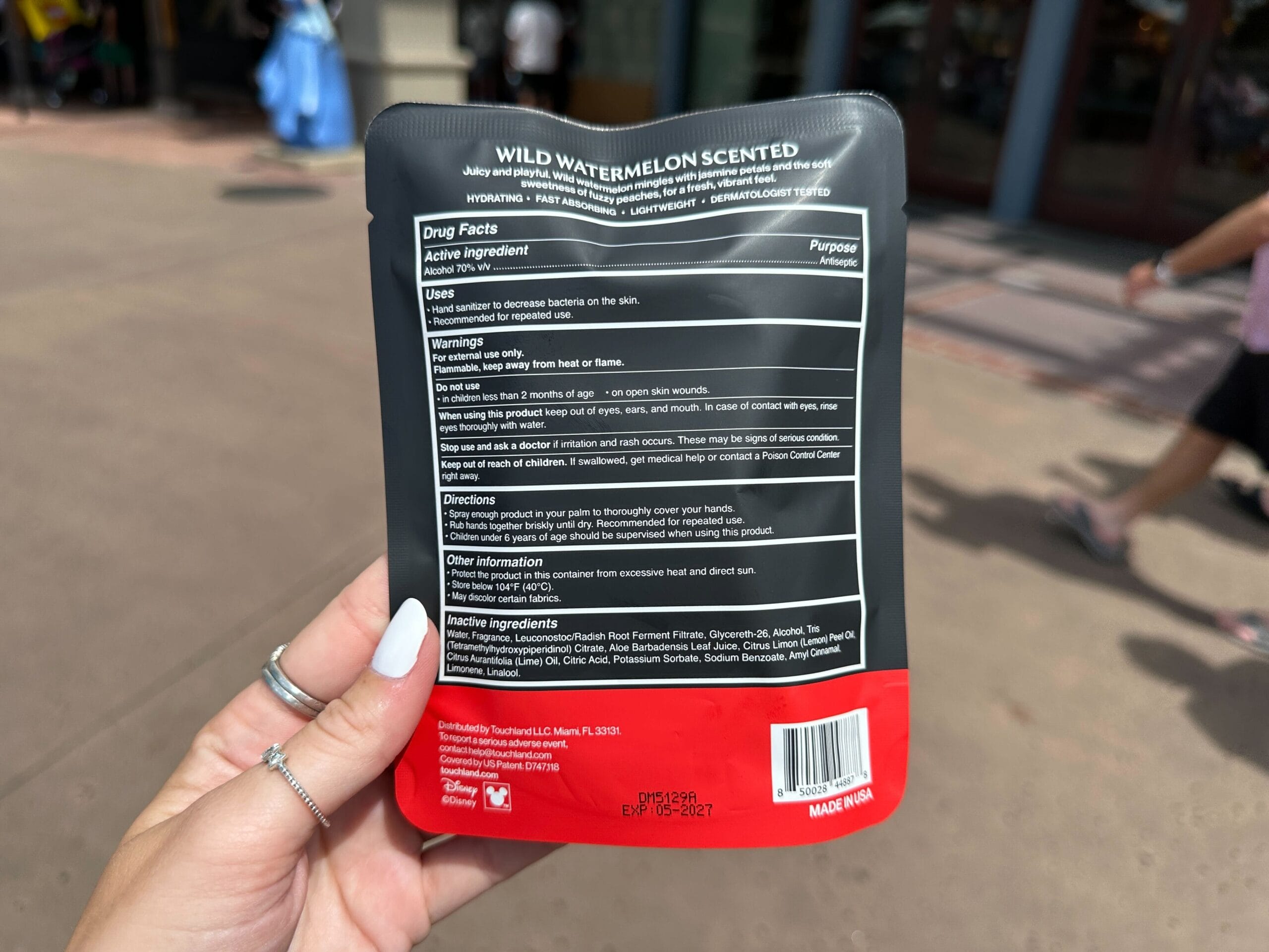 A hand holds a pouch of Wild Watermelon Scented wipes, showing the drug facts and directions on the back label.