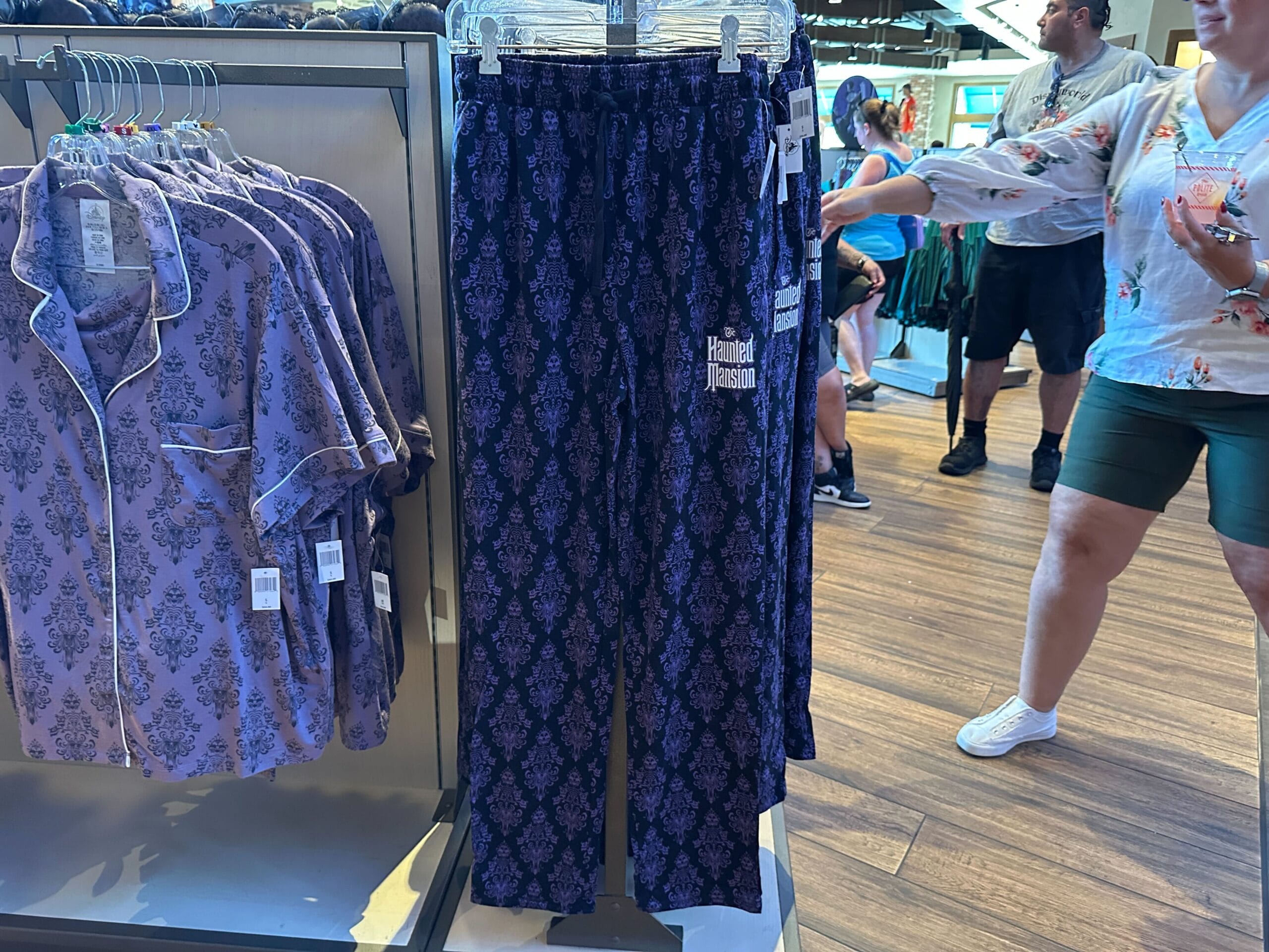 Purple pajama pants with a dark pattern, inspired by new Haunted Mansion items, hang beside matching tops in a busy store.