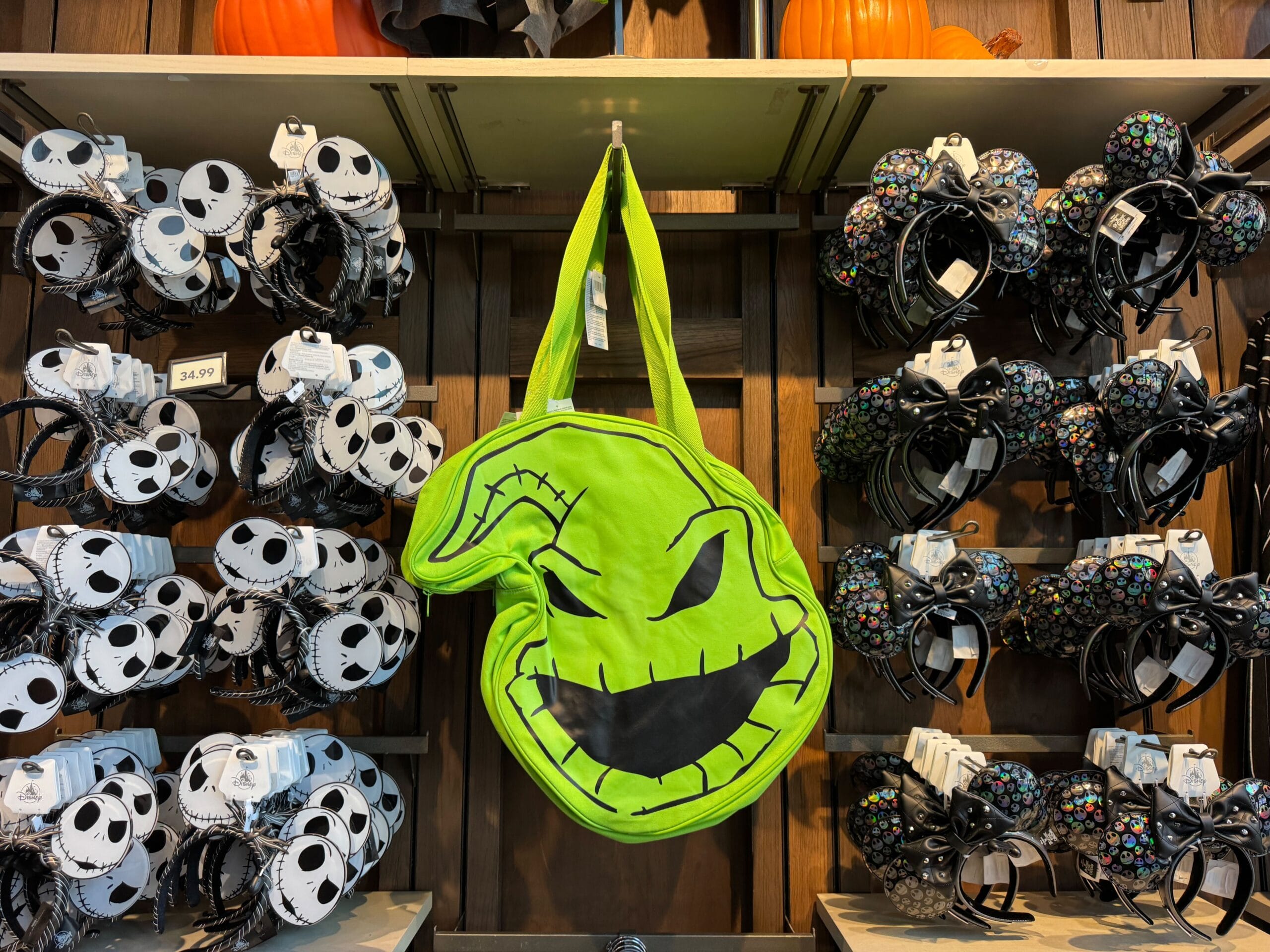 A bright green Oogie Boogie bag hangs on a wooden wall, surrounded by Jack Skellington and Minnie ear headbands.