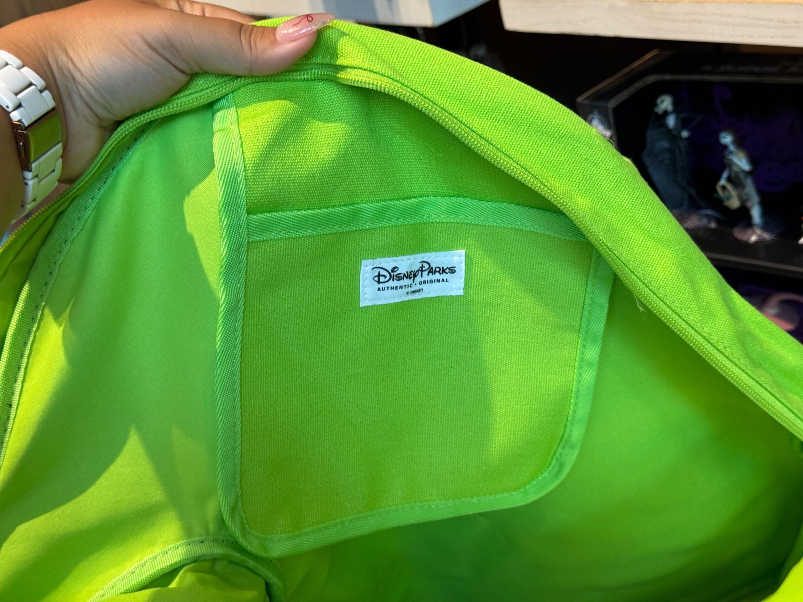 A hand holds open a bright green jacket, showing a "Disney Parks Authentic Original" label inside.