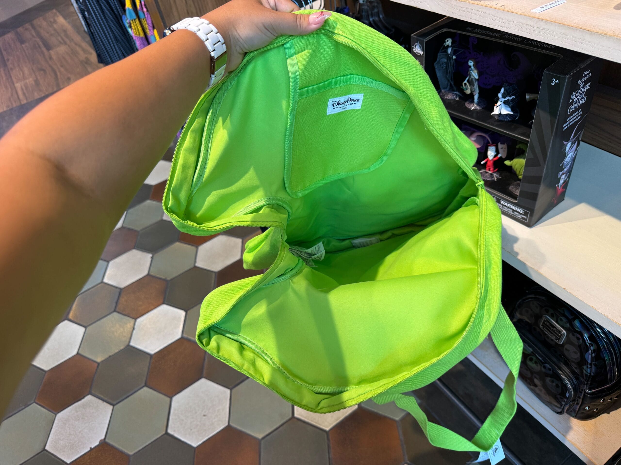 A person holds open a bright green shoulder bag in a store, showing its empty interior.