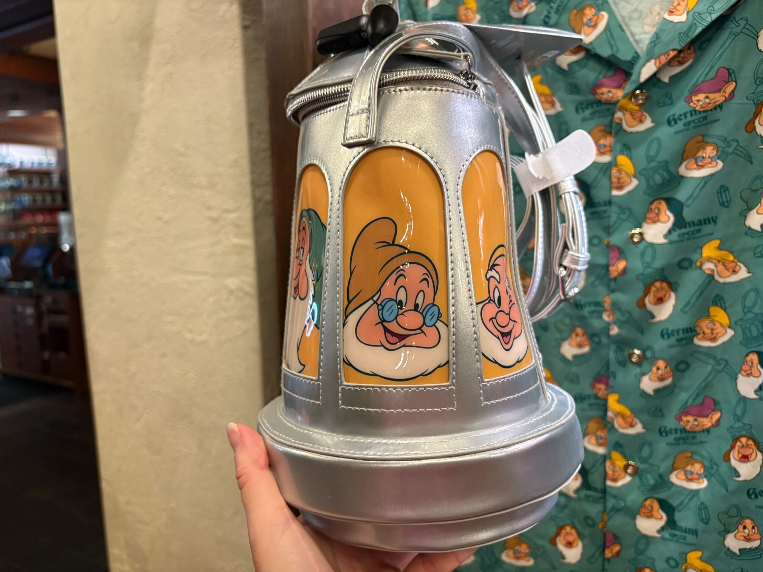 A hand holds a Seven Dwarfs stein bag; a matching shirt hangs in the background.