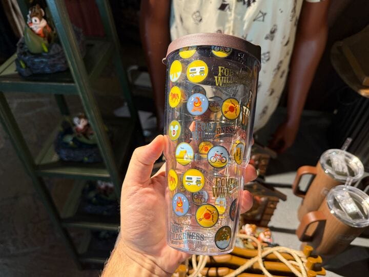 A hand holds a clear tumbler decorated with Disney’s Fort Wilderness merchandise and colorful adventure-themed stickers.