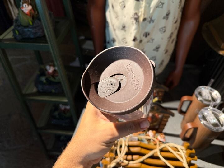 A hand holds a Tervis travel tumbler with a brown lid featuring a smiling bear face—new Disney’s Fort Wilderness merchandise.