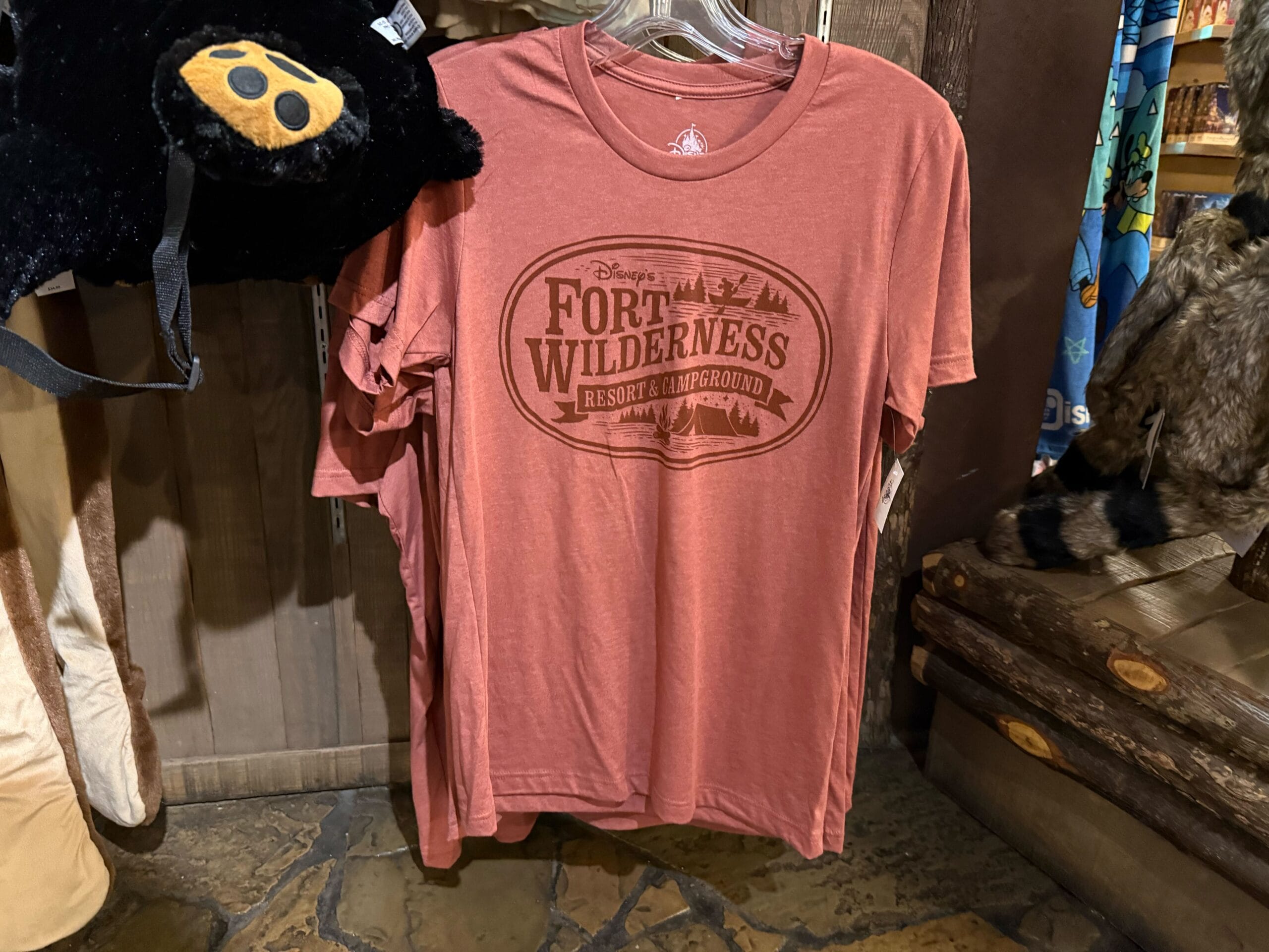 A red Disney’s Fort Wilderness resort T-shirt hangs on display in a rustic-themed merchandise store.